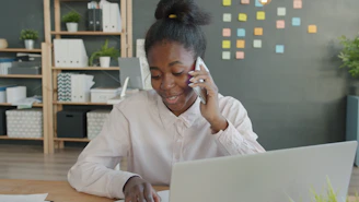 Young woman talking on phone at office desk with laptop