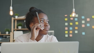 Young woman holding pencil, thinking at desk.
