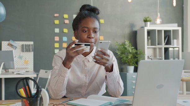 Woman holding credit card and phone at desk.