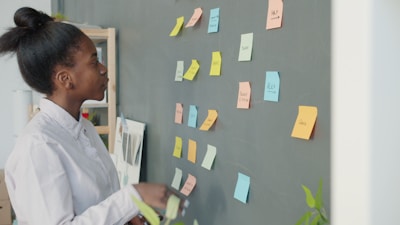 Young woman reviewing colorful sticky notes on wall.