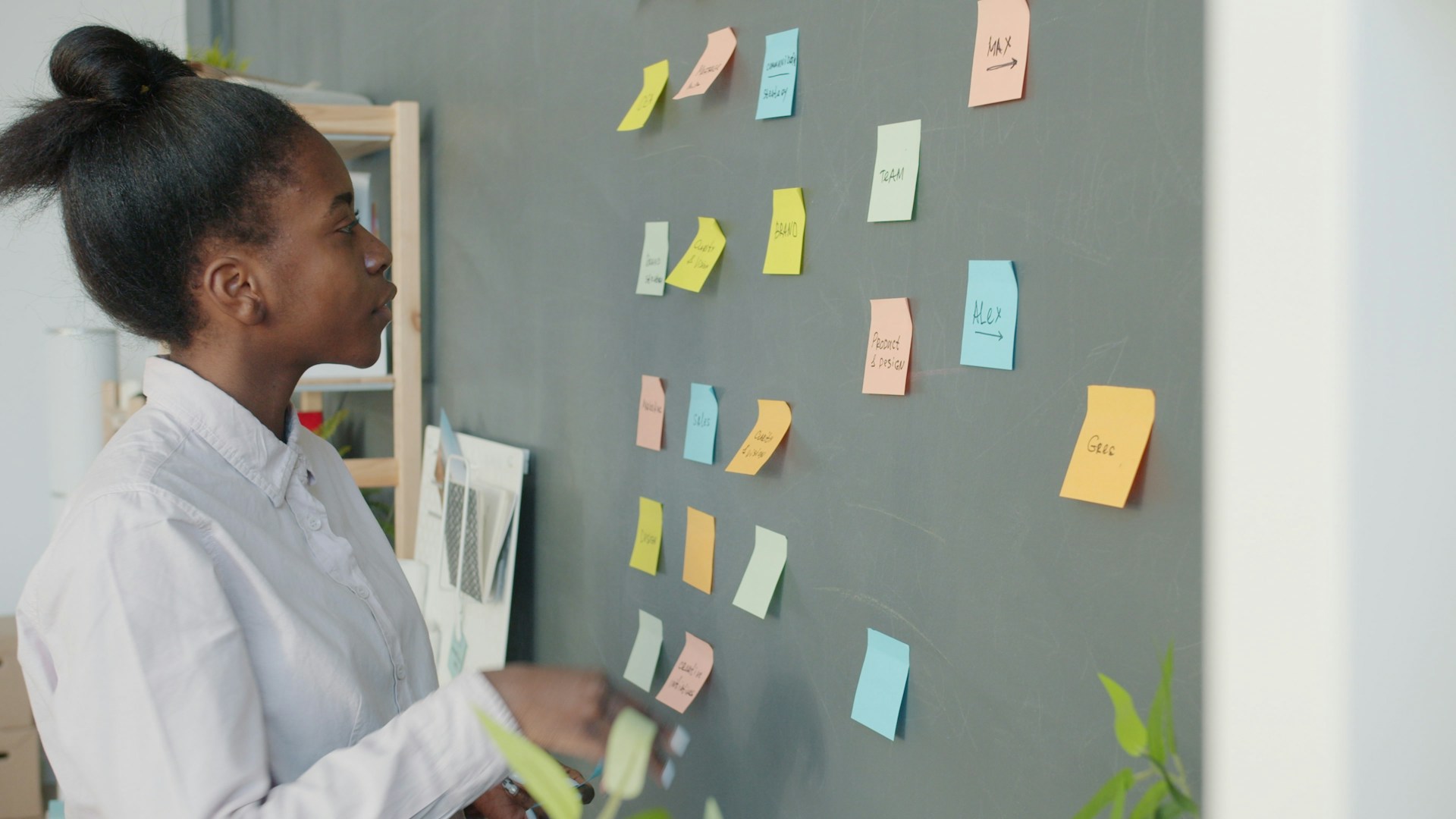 Young woman reviewing colorful sticky notes on wall.