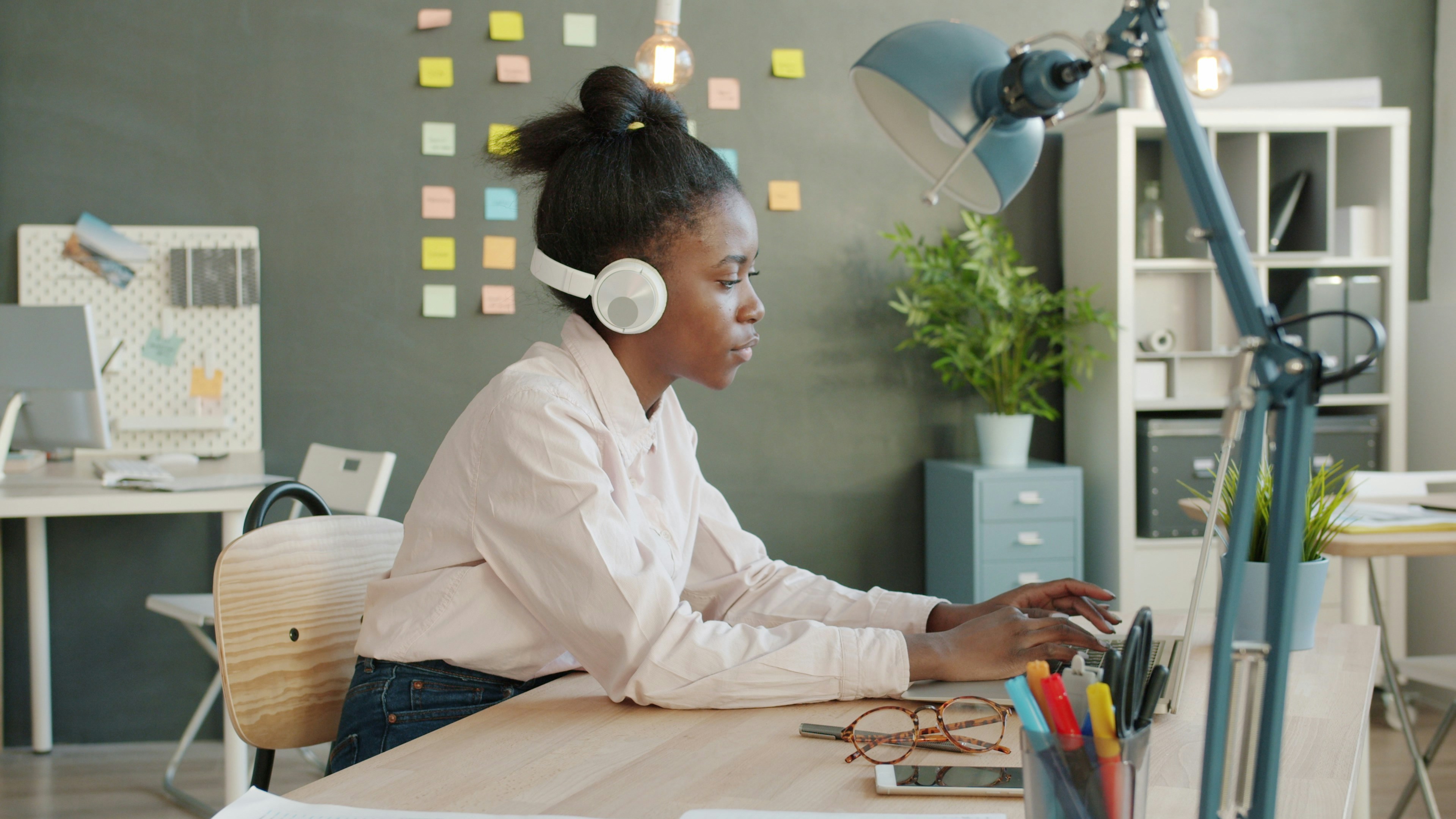 Woman wearing headphones working on laptop at desk.