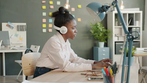 Woman wearing headphones working on laptop at desk.