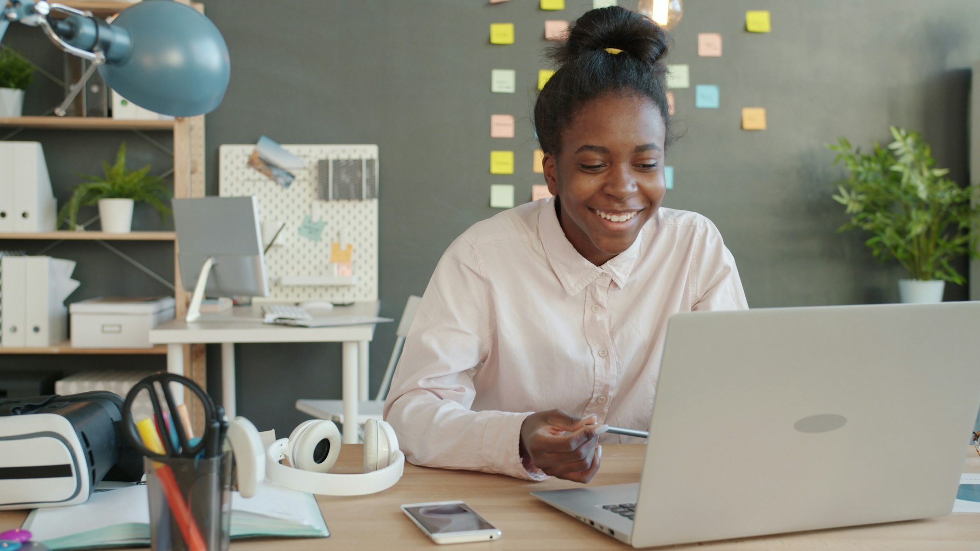 Smiling woman taking notes at a desk during an online MBA class on her laptop
