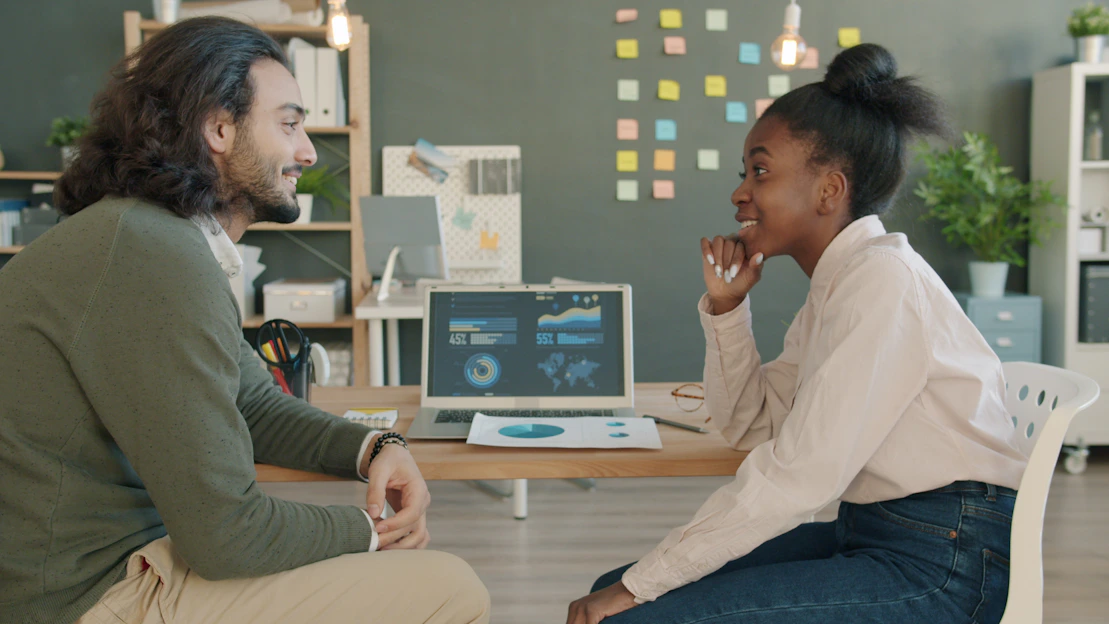 Two colleagues discussing work at a desk.