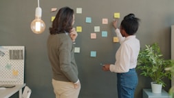 Two people brainstorming with sticky notes on wall.