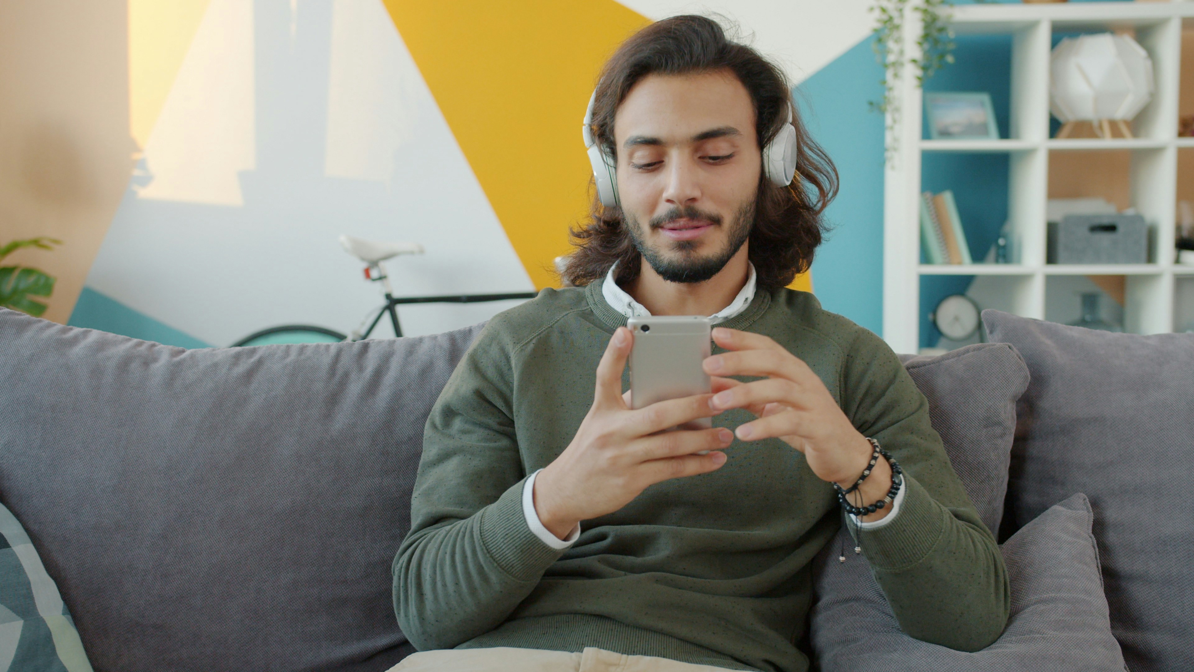 Man with headphones using smartphone on couch.