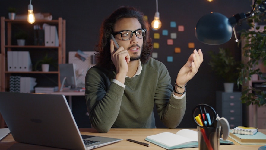 Man talking on phone at desk with laptop.