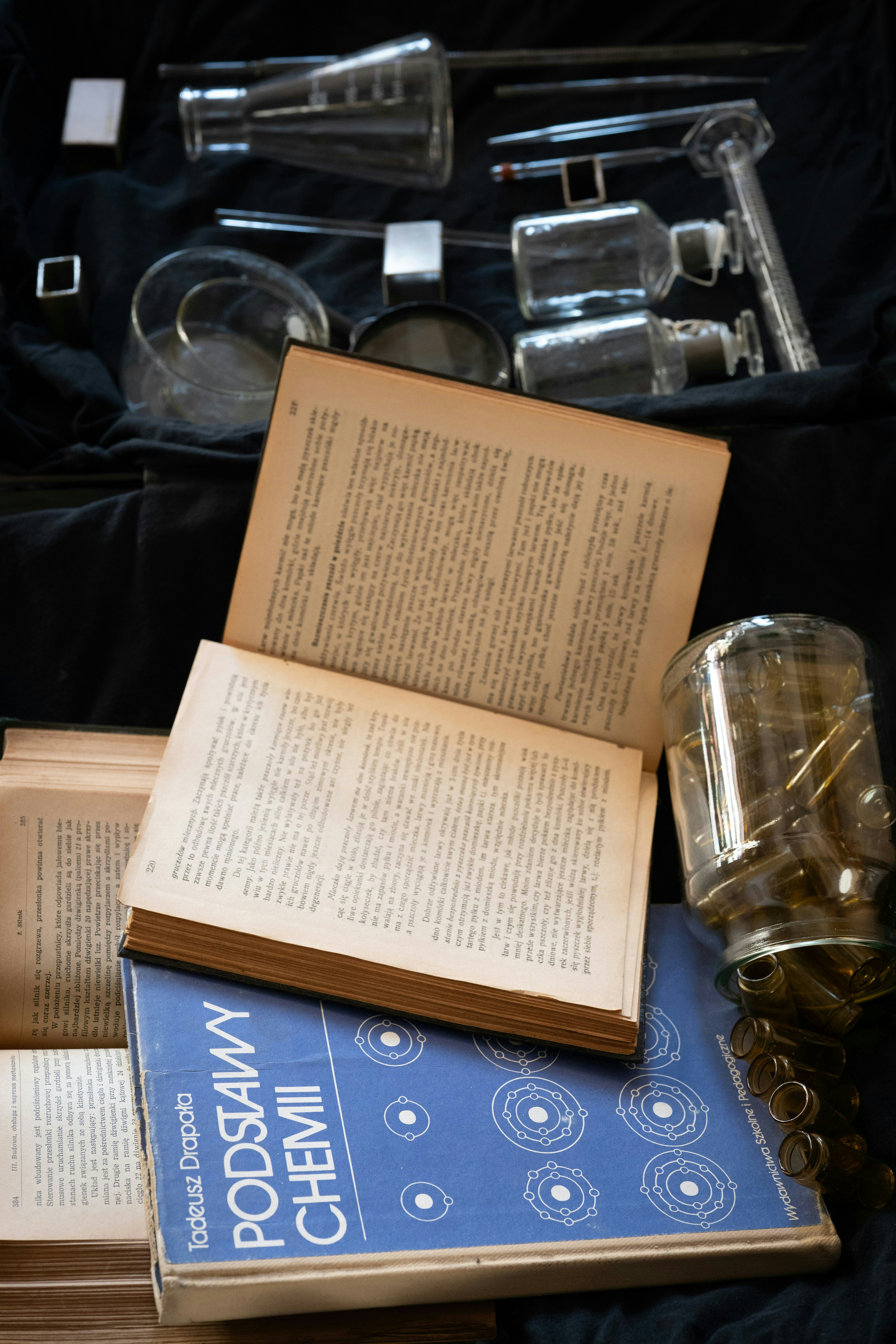 Old chemistry books and scientific glassware on dark fabric