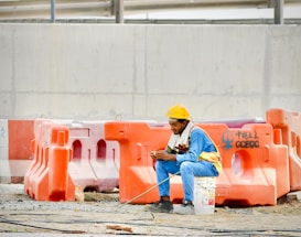 Construction worker in hard hat sits on bucket using phone.