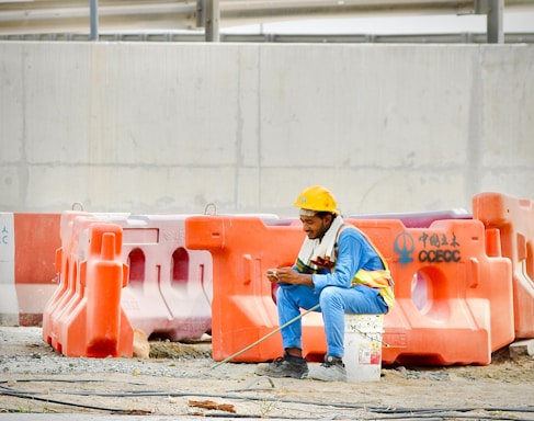 Construction worker in hard hat sits on bucket using phone.