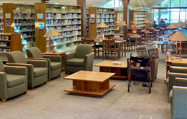 A public library seating area, with tables and chairs between rows of bookshelves