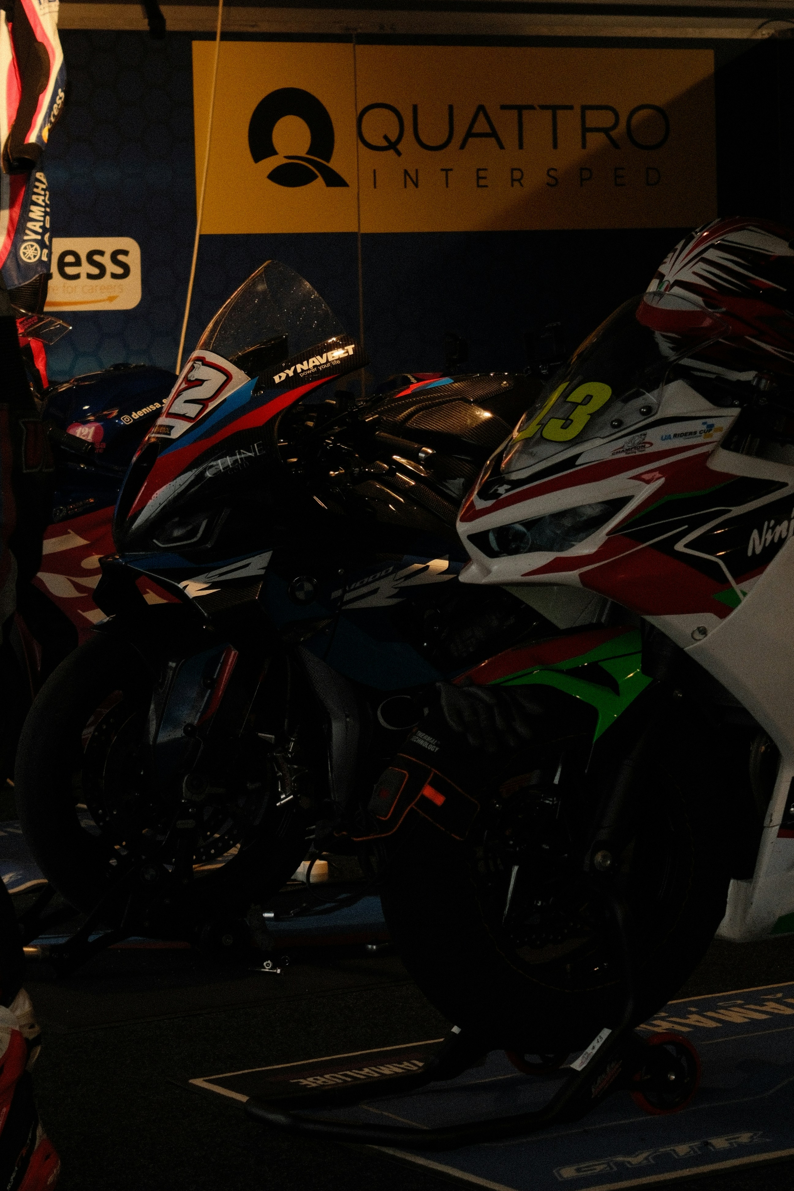 Two racing motorcycles parked indoors with logos.