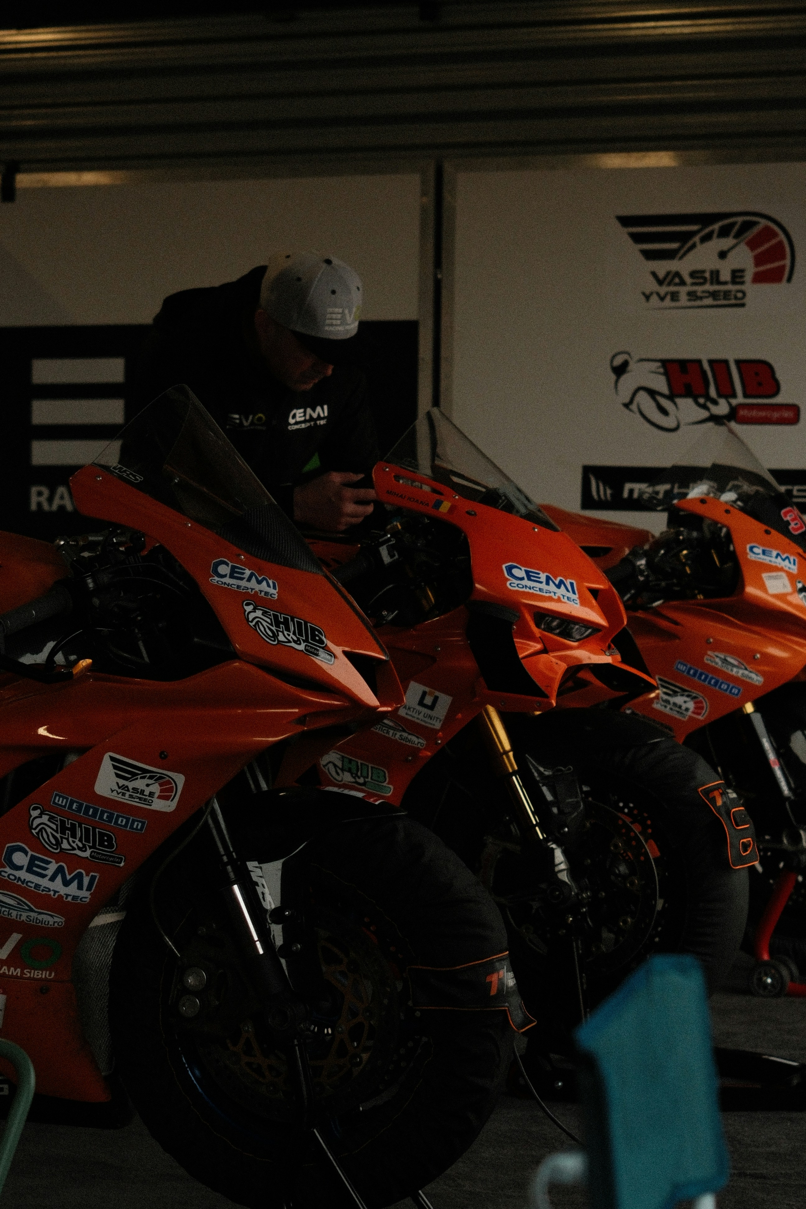 Mechanic working on orange racing motorcycles in garage.