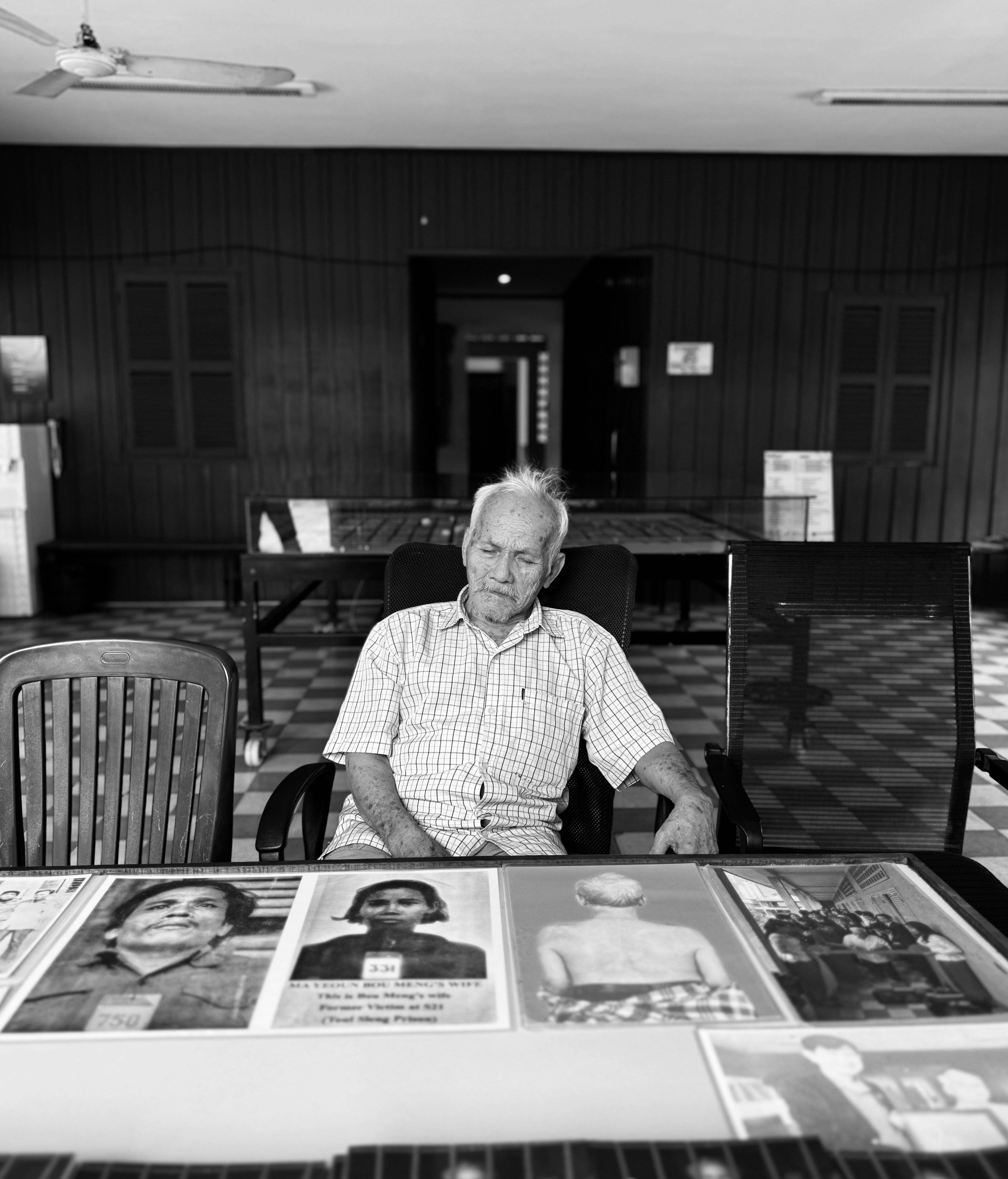 Elderly man sits in front of displayed portraits