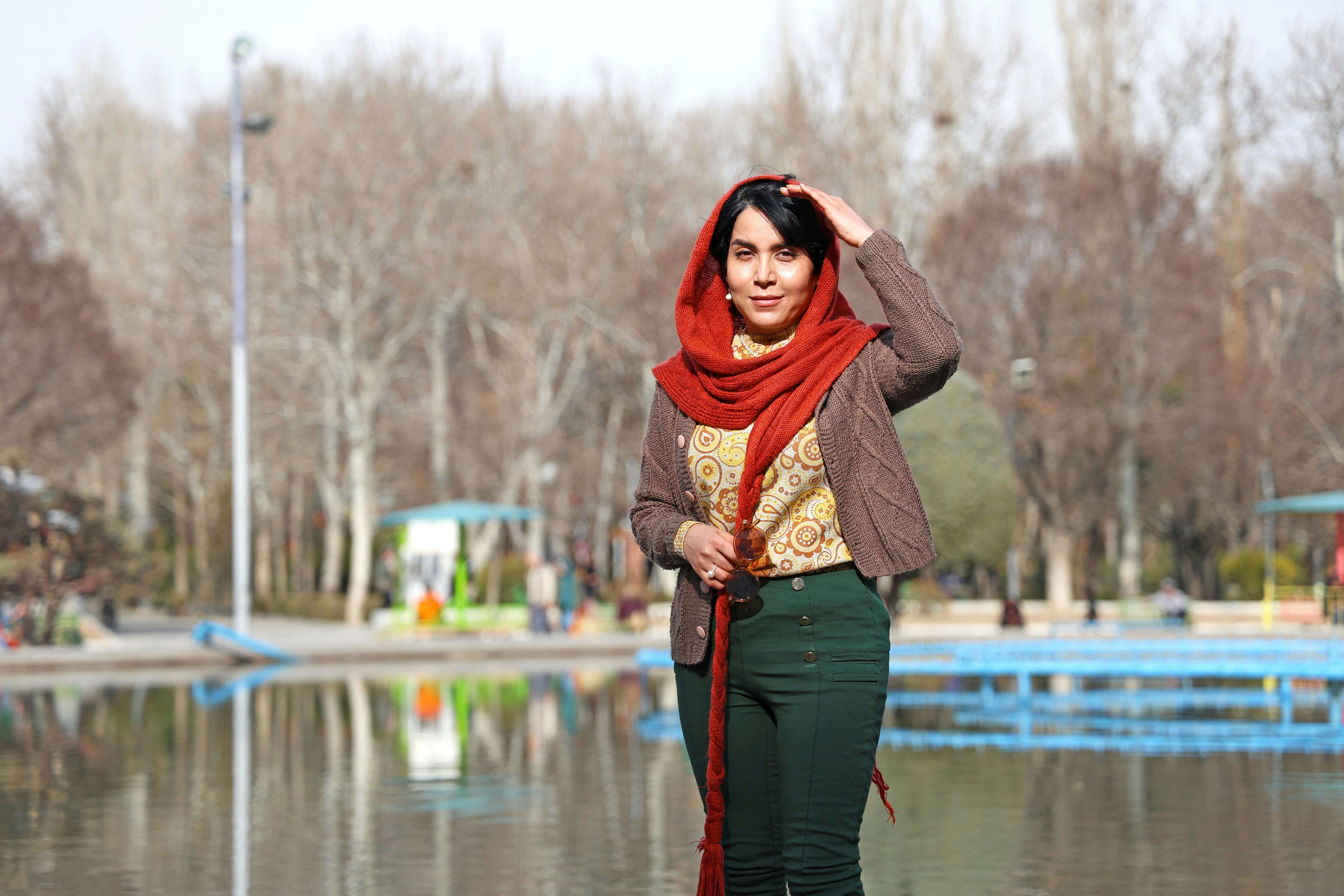Woman in red scarf stands by a park pond