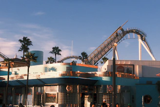 Roller coaster tracks curve over buildings and palm trees.