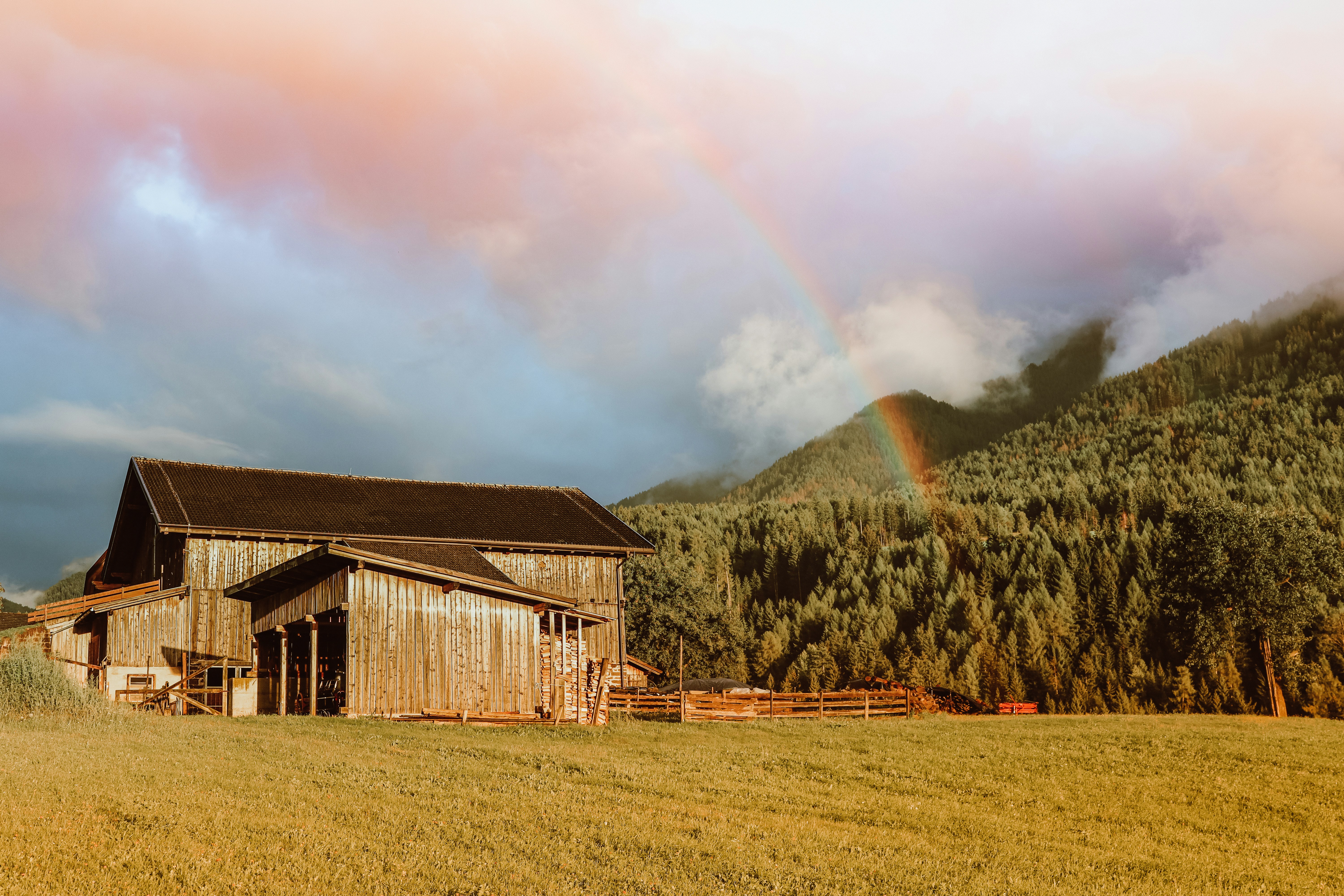 Rustic barn with rainbow over forested mountains