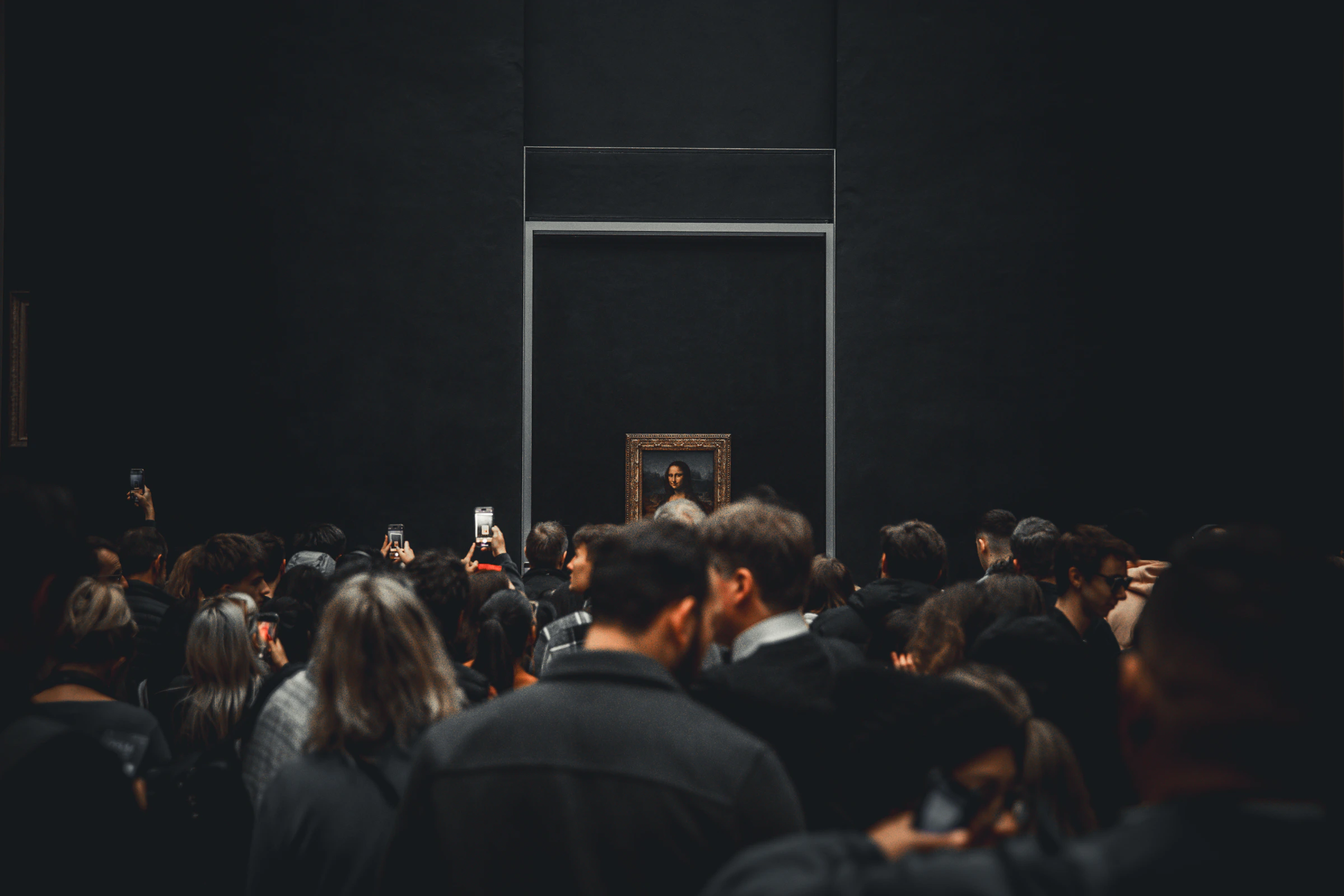 Crowd gathered before a painting in a dark museum hall