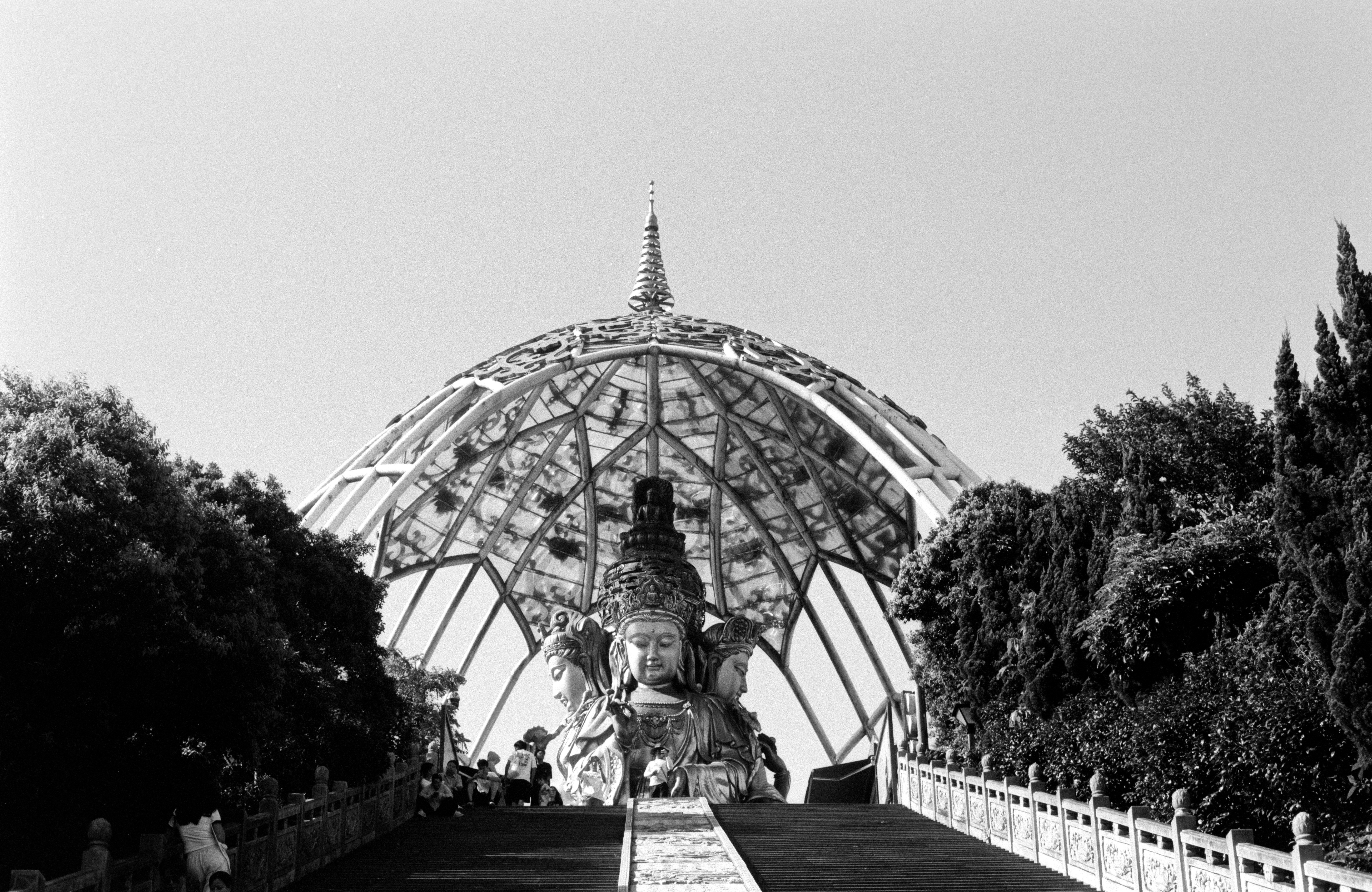 Statue under a geodesic dome with surrounding trees.