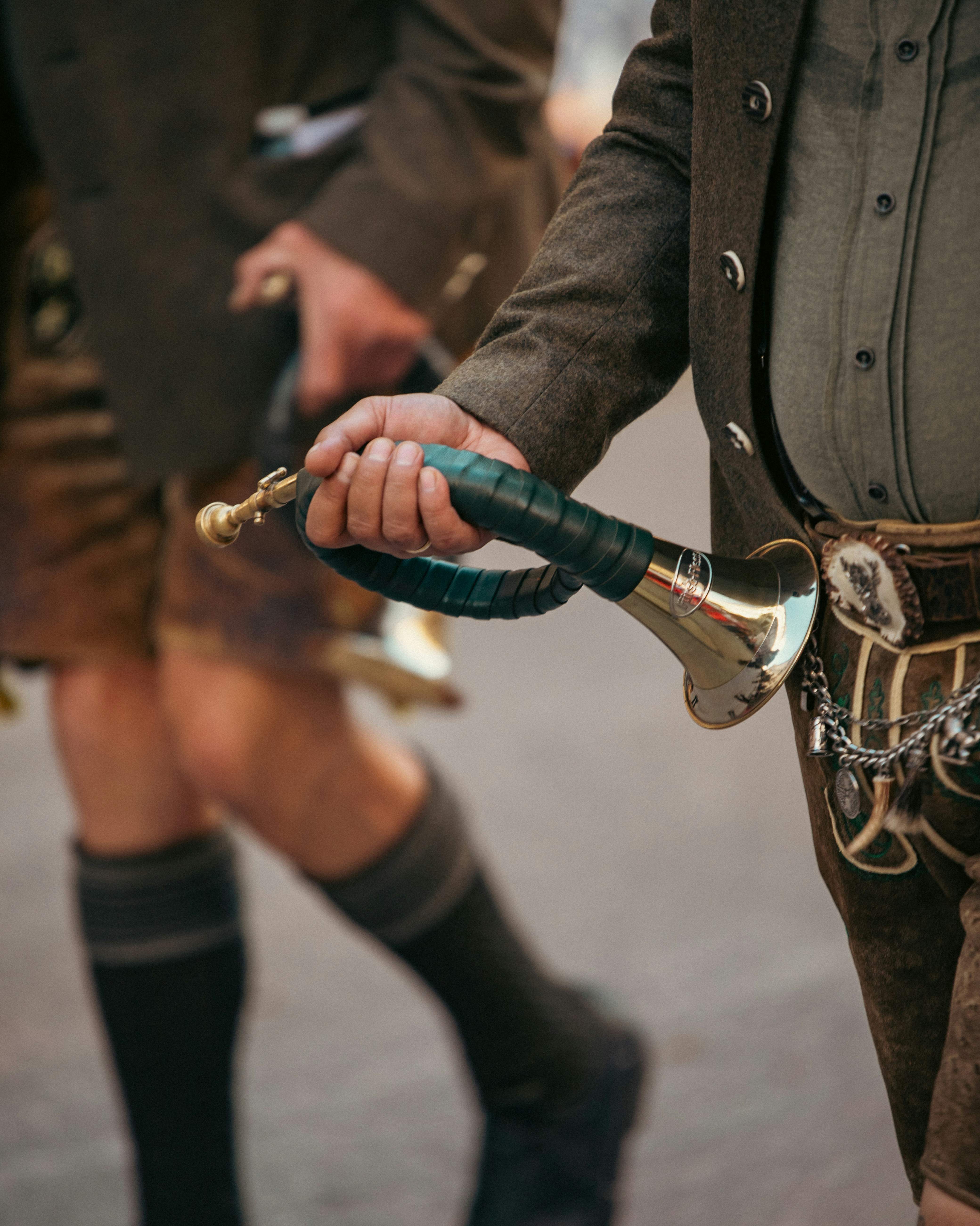 Man in traditional lederhosen holding a small brass horn