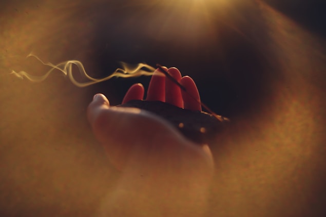 Hand holding burning incense with smoke rising.