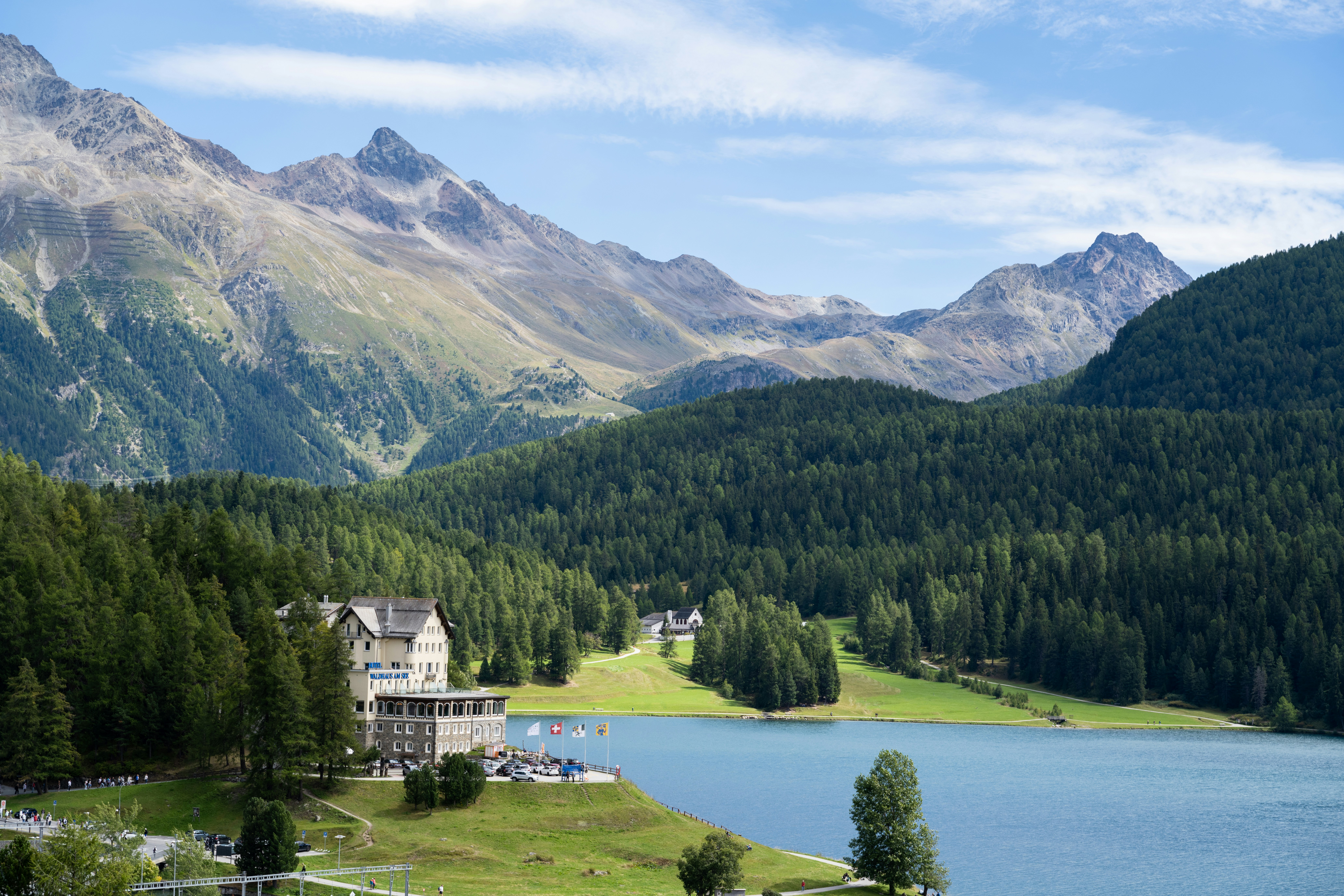 Grand hotel beside a serene lake and mountains.