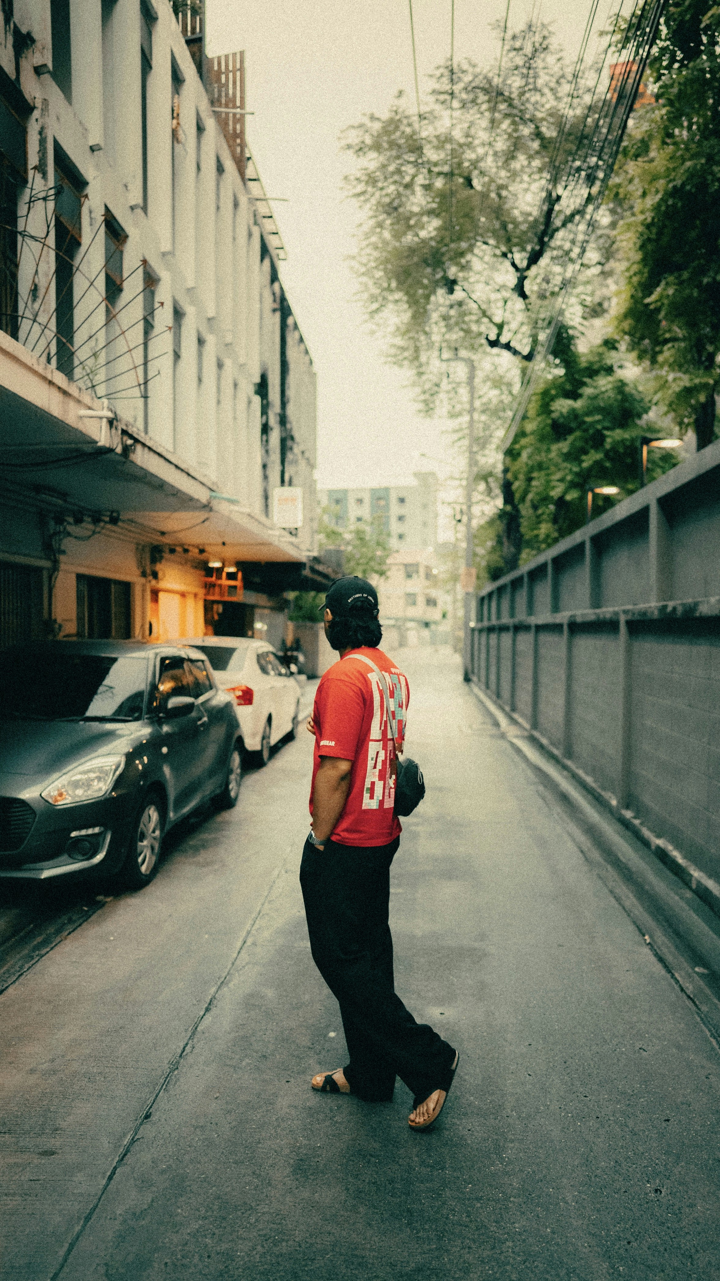 Man in red shirt walks down a narrow street.