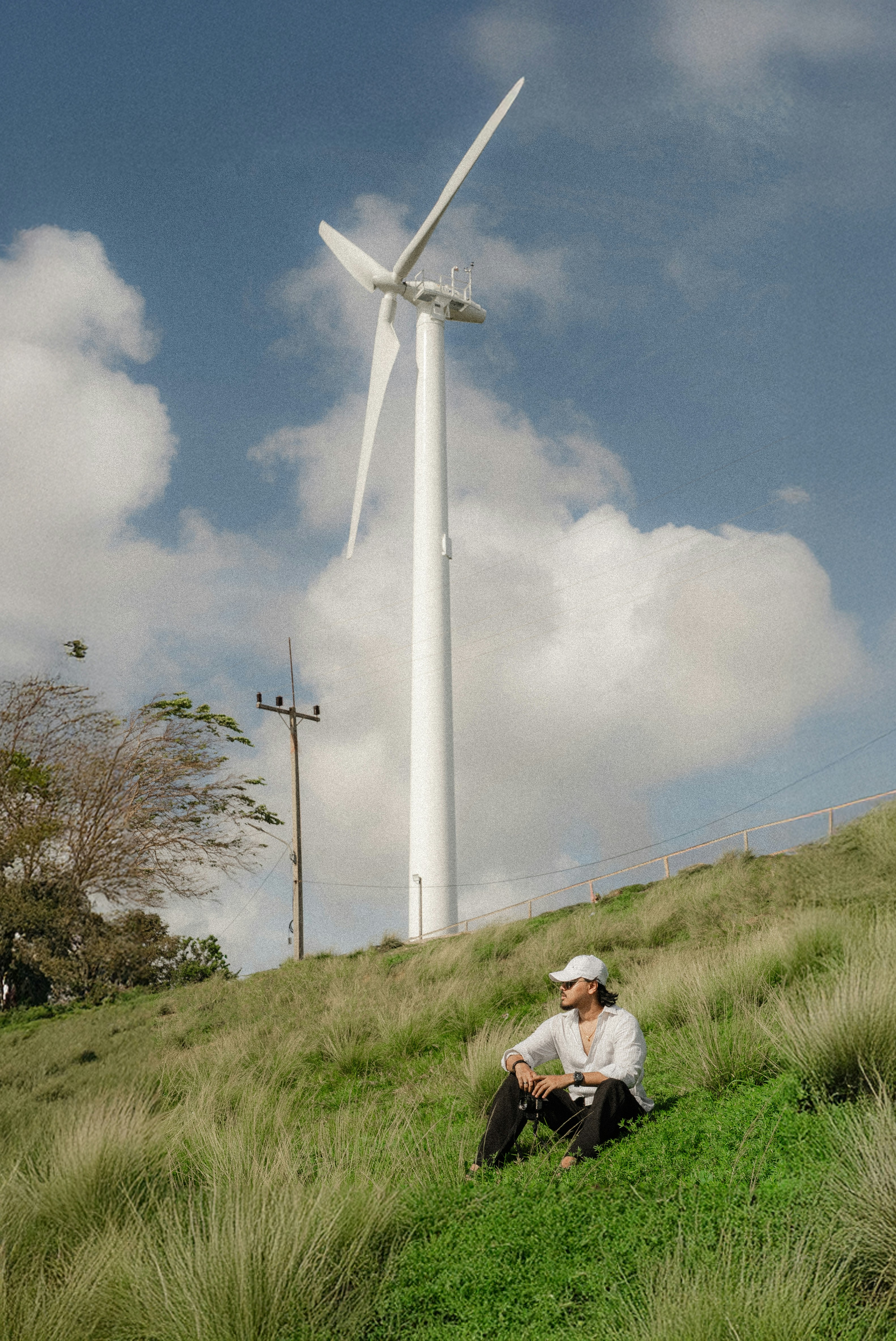 Man sits on grassy hill near a wind turbine.