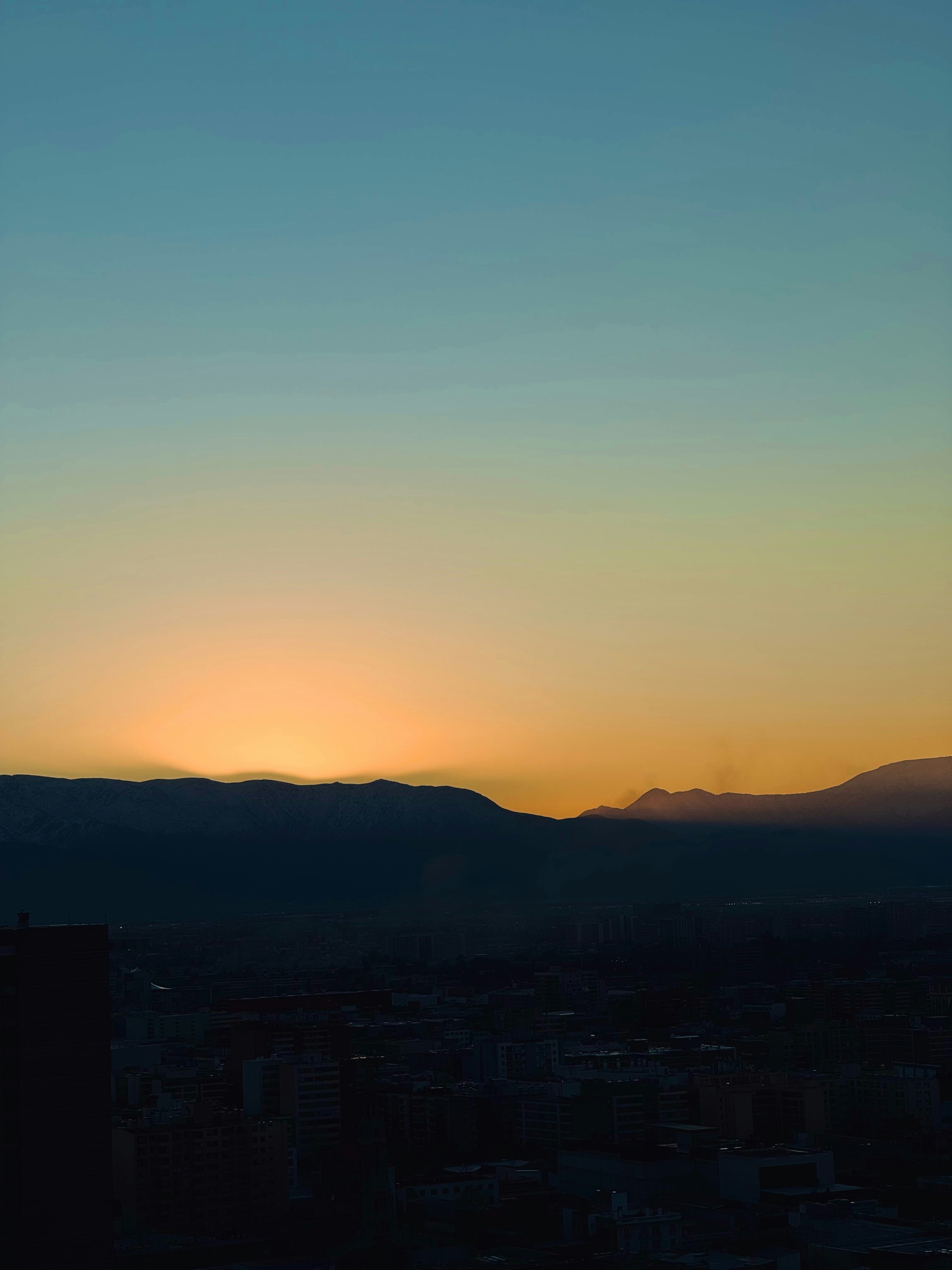 Sunset over distant mountains above a city.