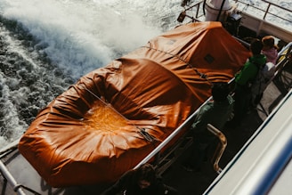 Orange life raft secured on a moving boat deck.
