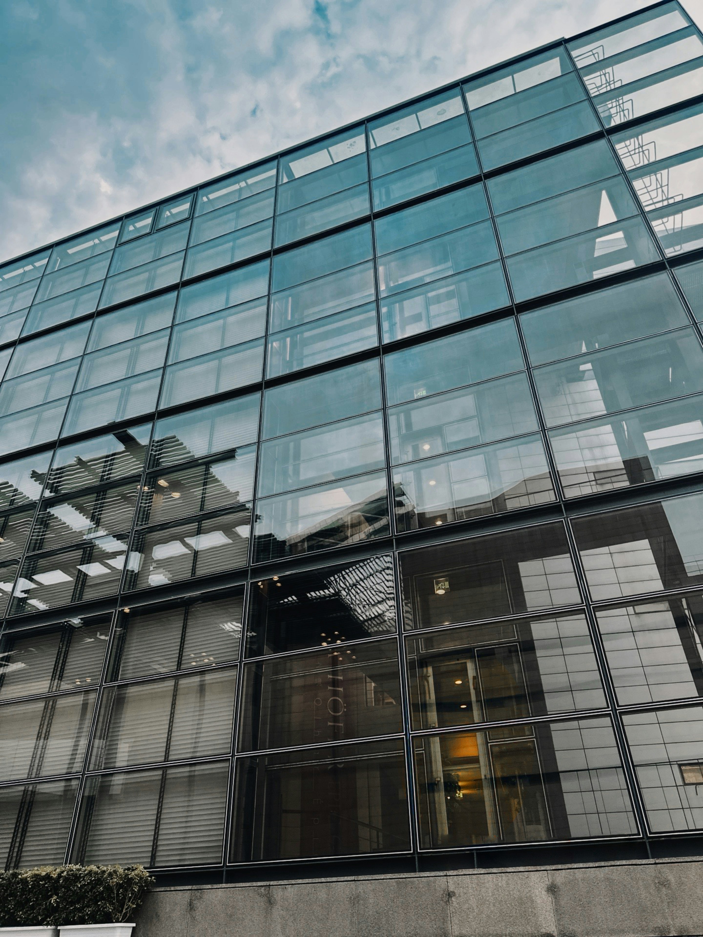 Modern glass building facade with reflections under cloudy sky