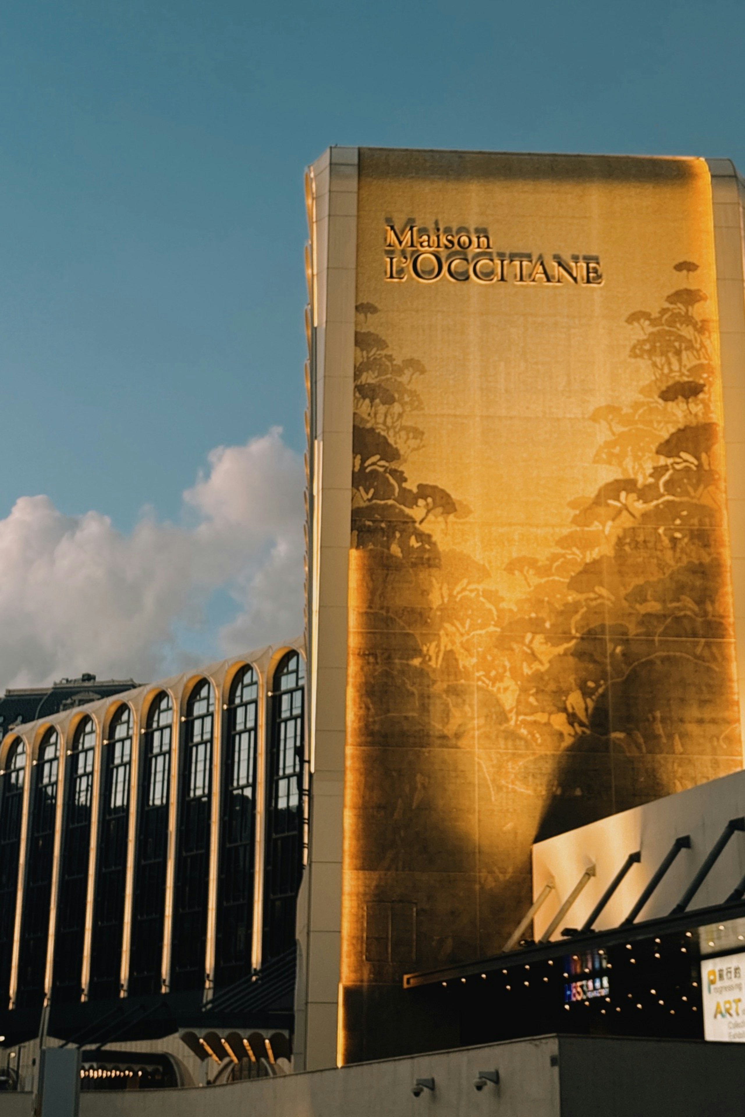 Golden building facade with l'occitane logo and trees.