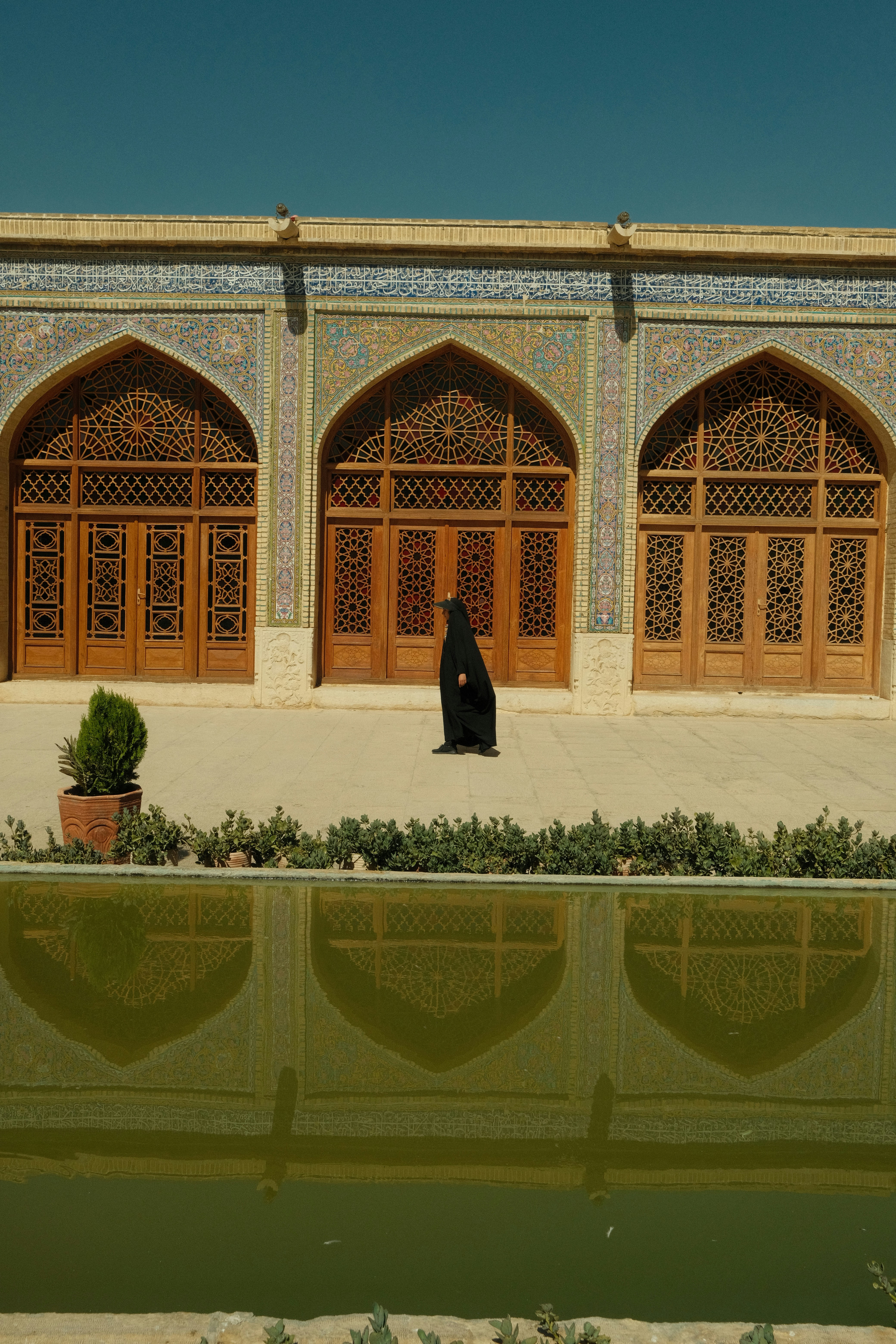 Woman in black walks in front of ornate mosque doors