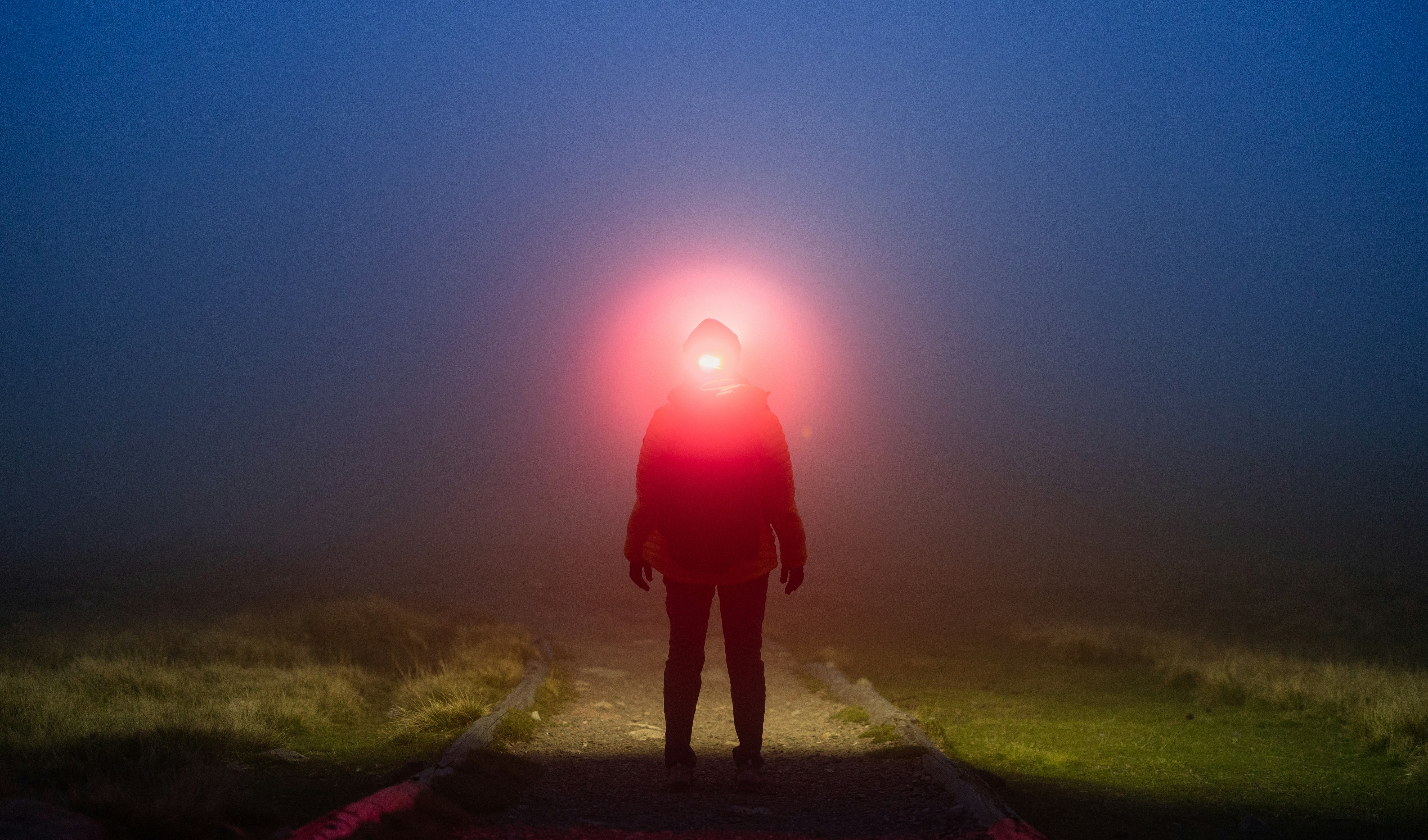 Person with red headlamp in foggy night landscape