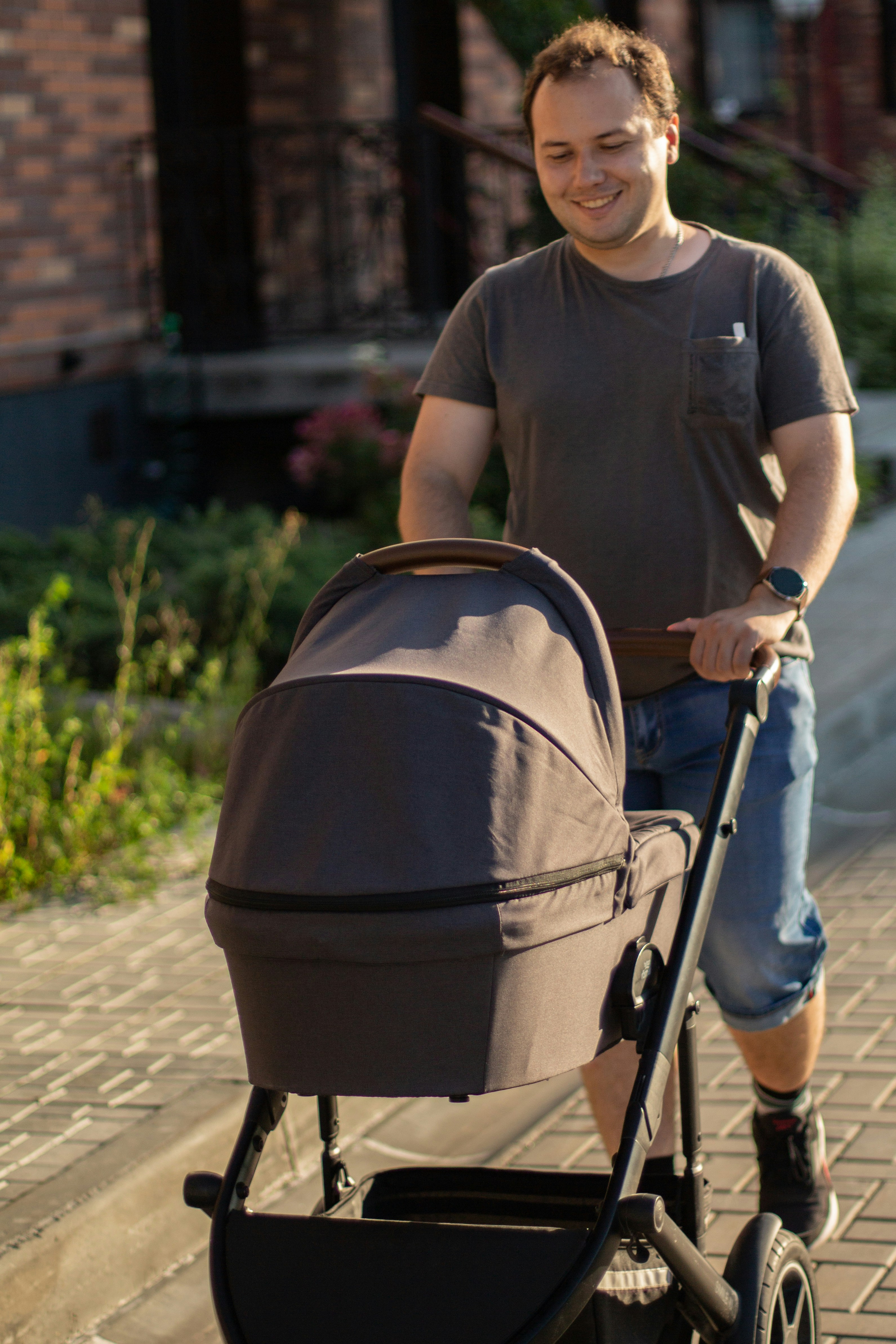 Mann schiebt einen Kinderwagen auf einen gepflasterten Weg.