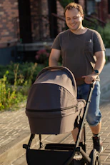Man pushing a baby stroller on a paved path.