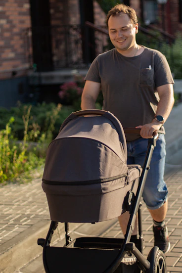 Man pushing a baby stroller on a paved path.