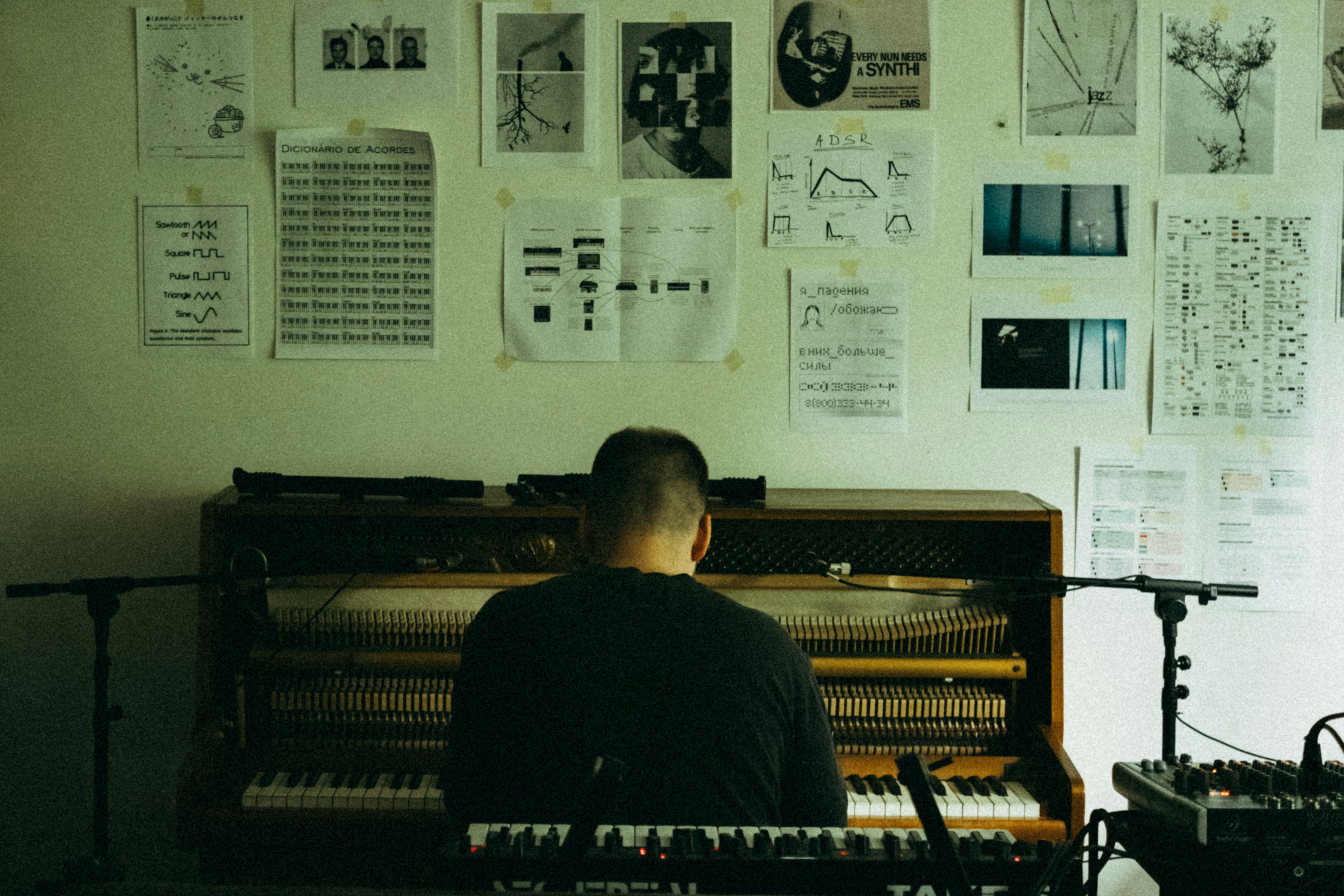 Man playing piano with sheet music on wall.