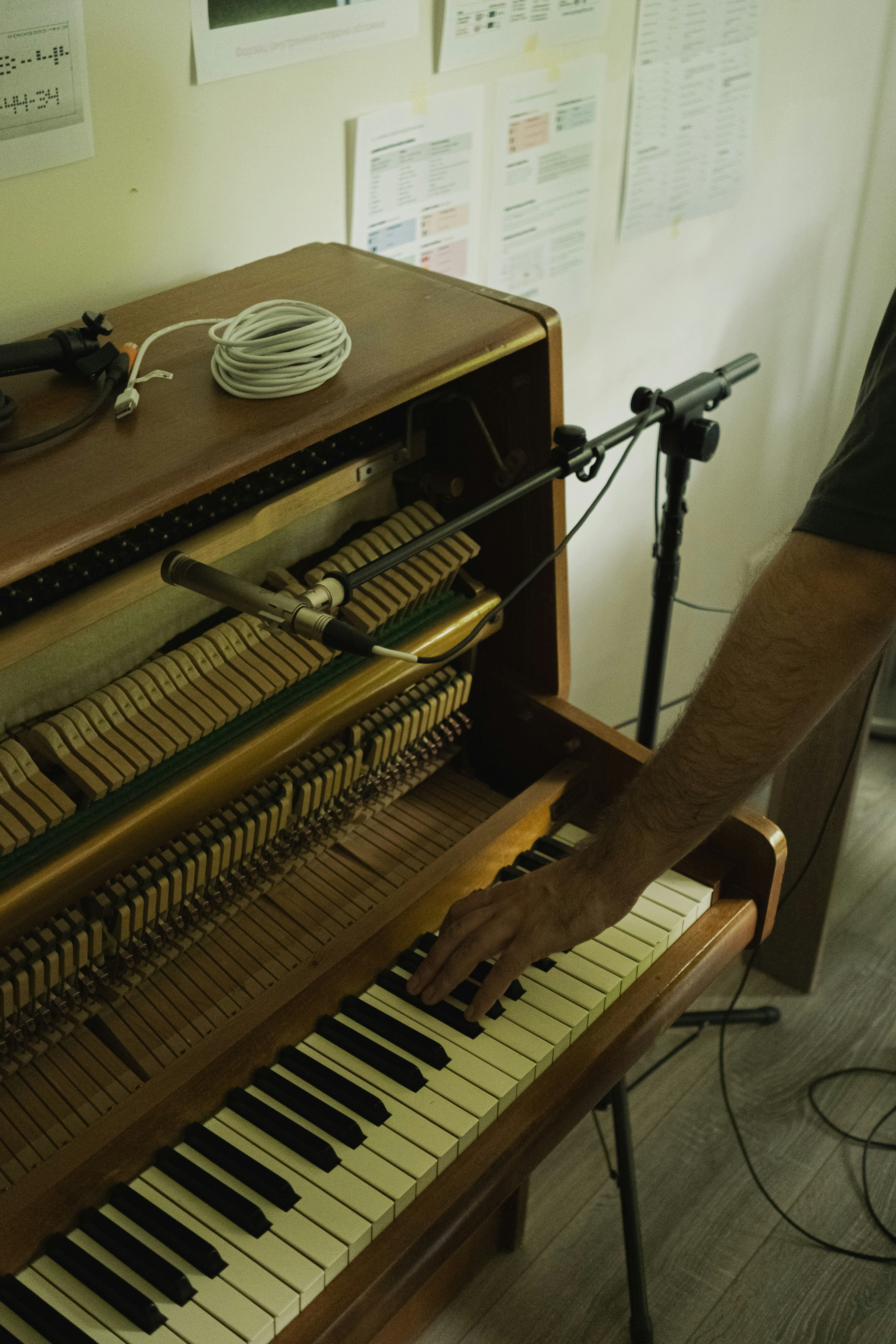 Hand playing an upright piano with microphone setup