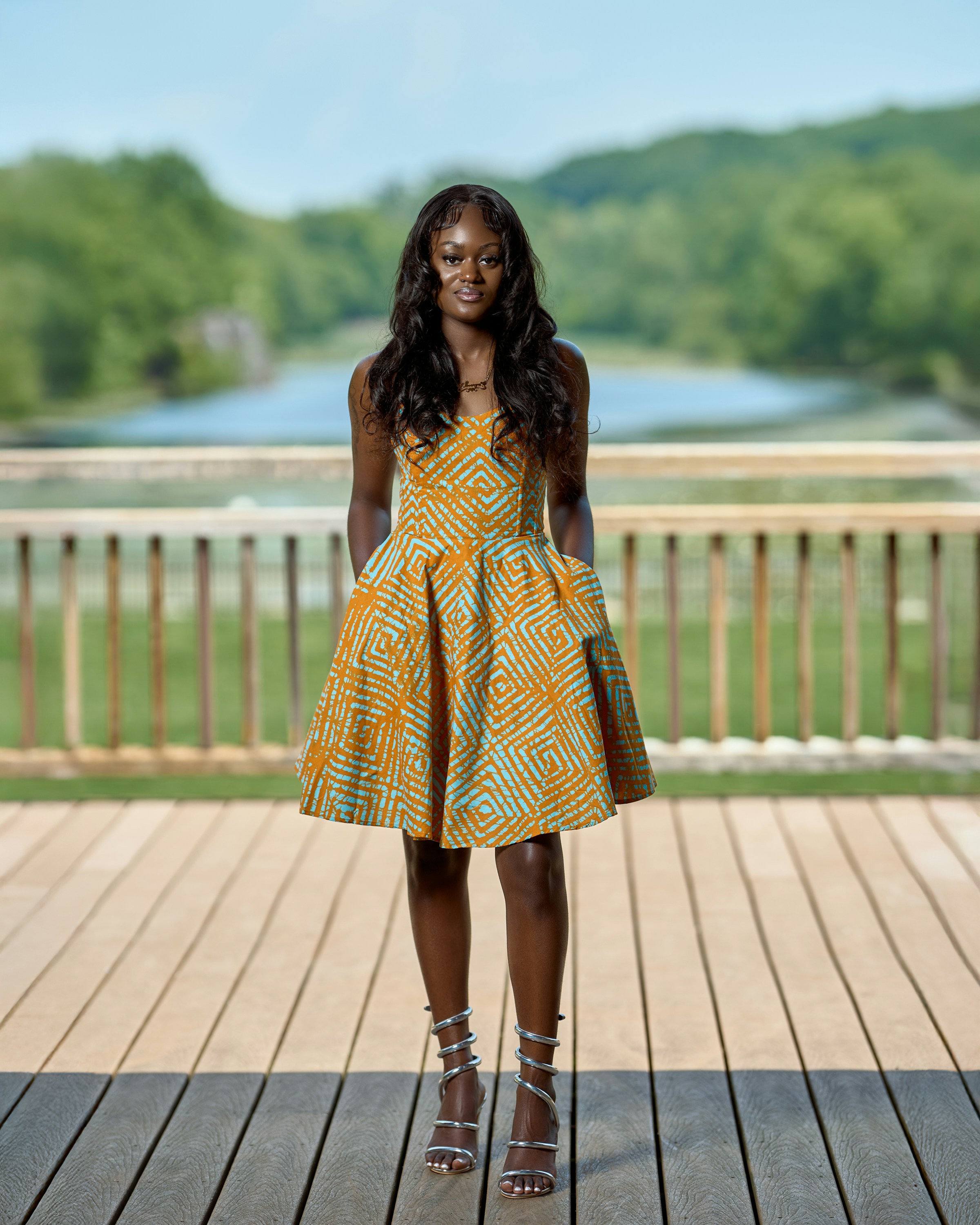 Woman in patterned dress stands on wooden deck by water