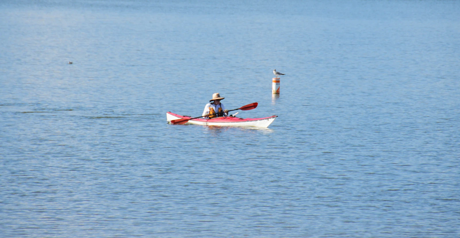 Solo paddler in a sit-inside kayak crossing a calm, glassy lake