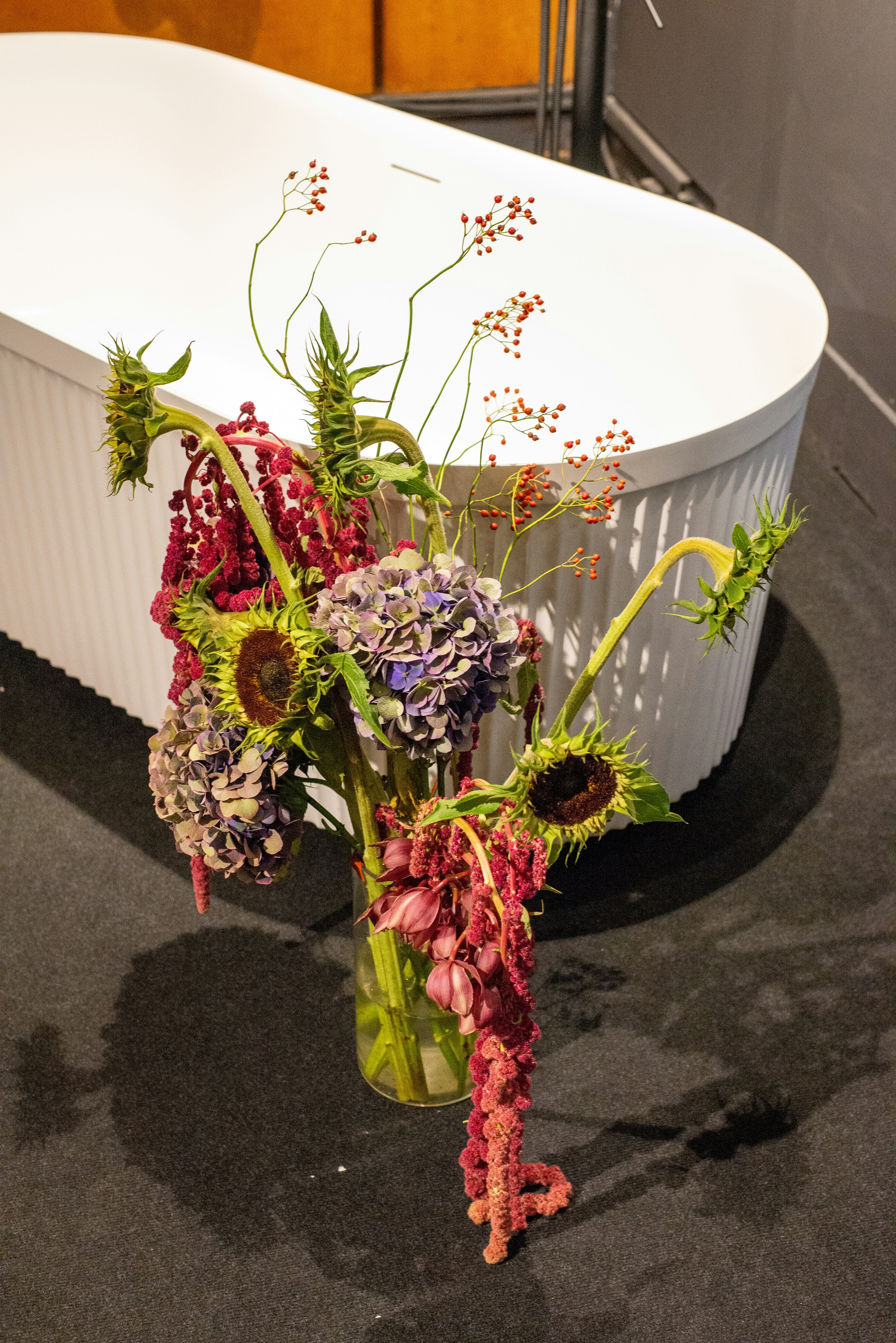 A vase of sunflowers and hydrangeas with red berries.