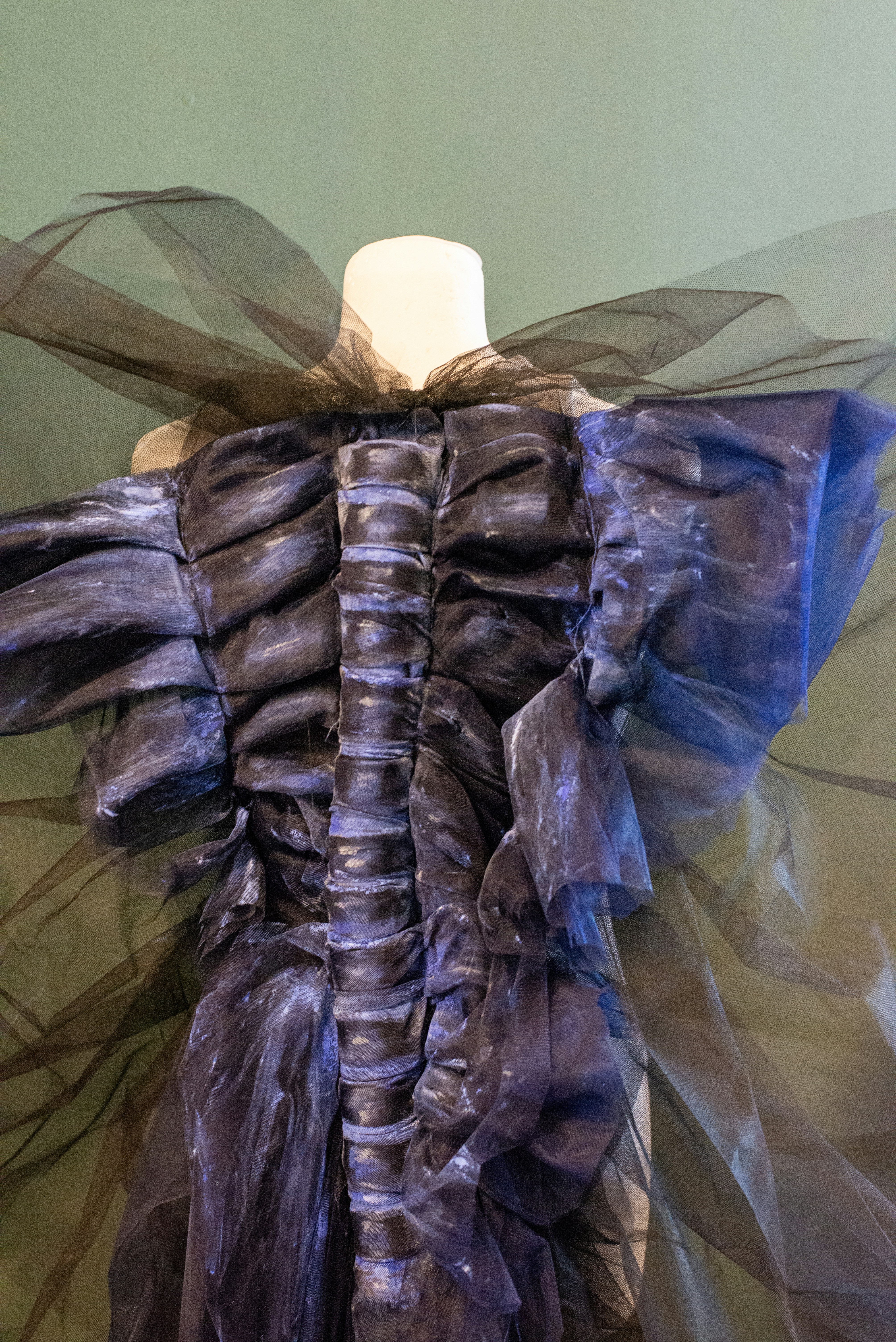 A dark, textured gown with sheer sleeves and collar.