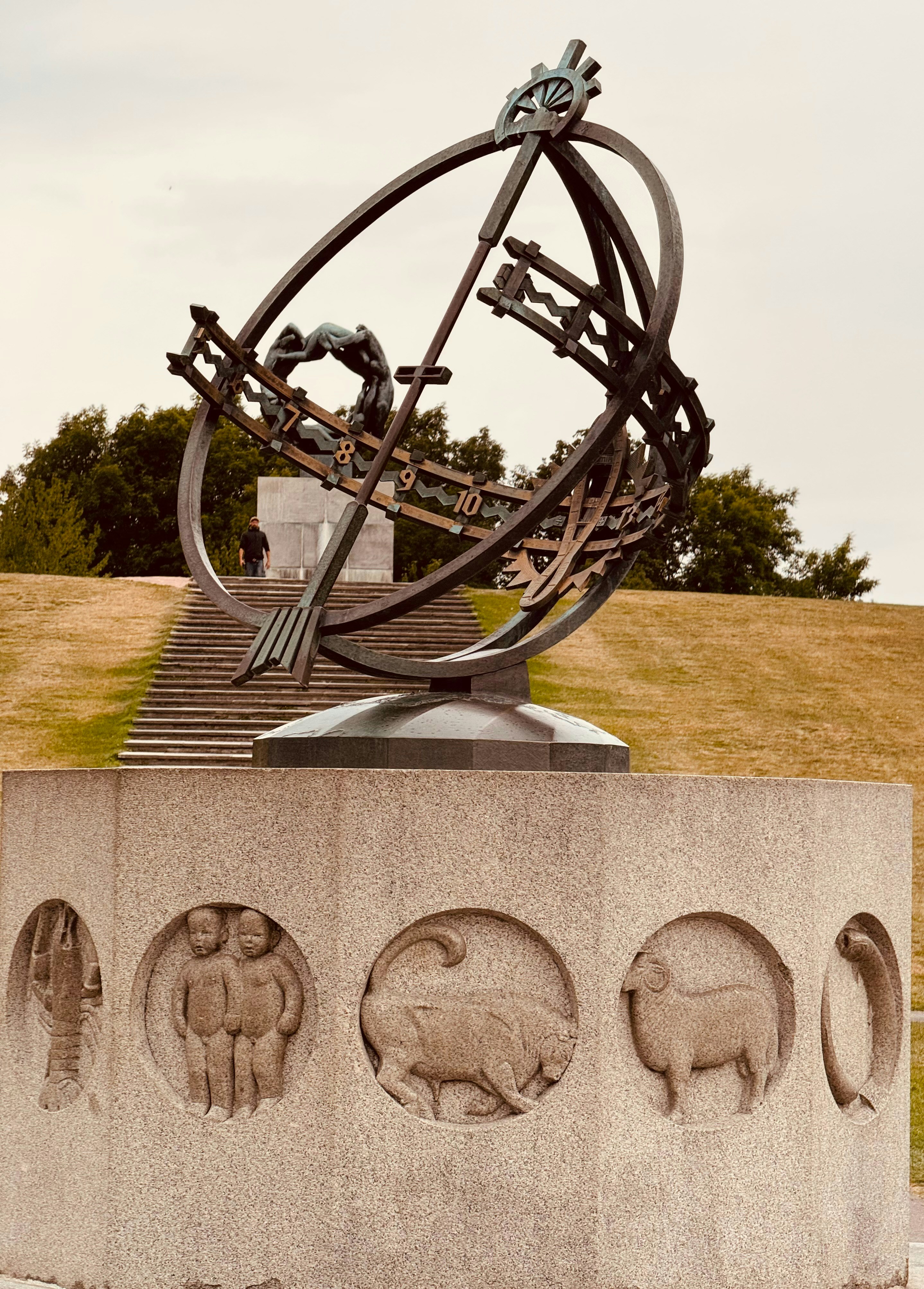 Große Metallskulptur mit Tierkreiszeichen auf Sockel.