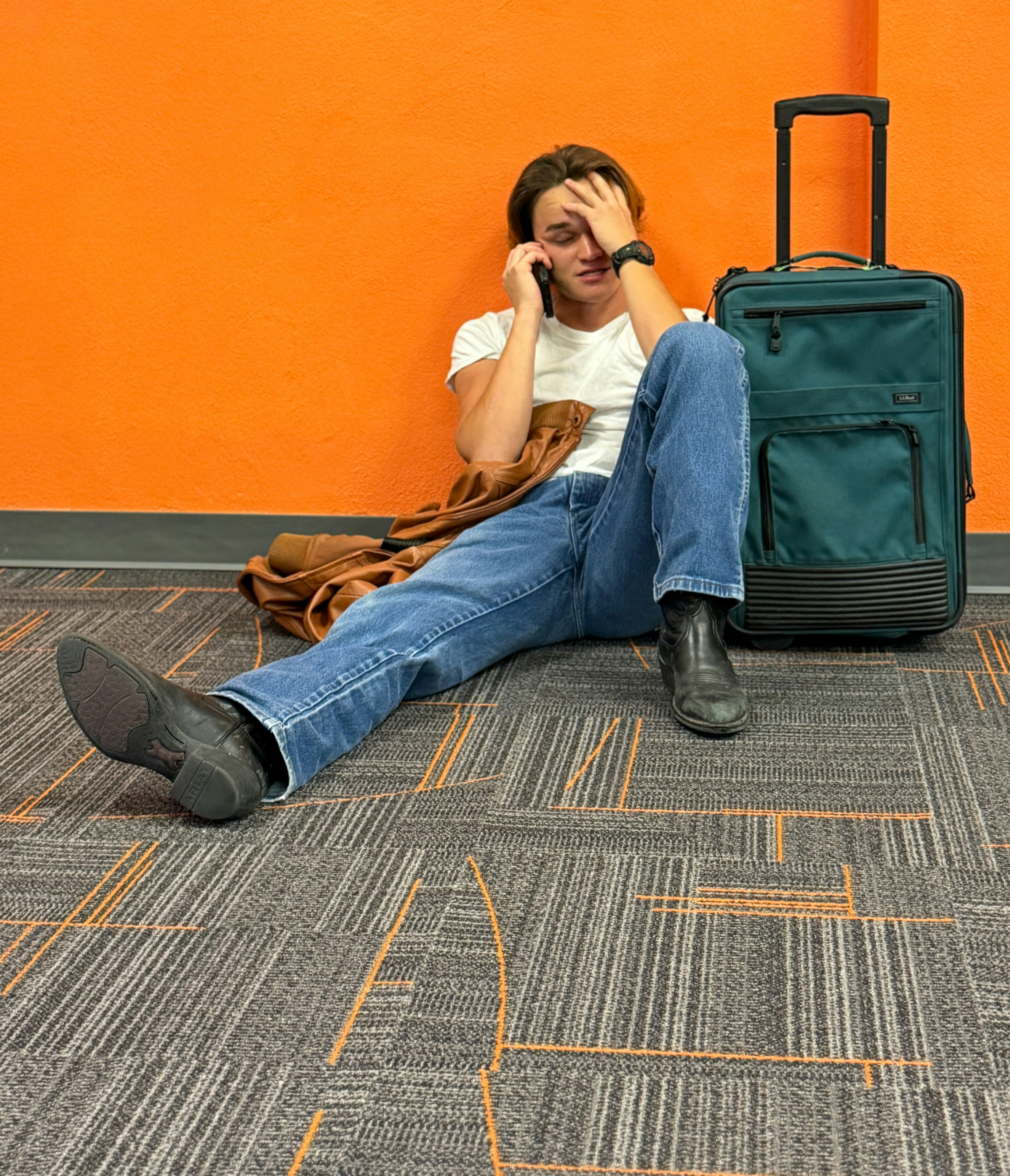 Exasperated Young man with suitcase sitting on the floor waiting for his flight.