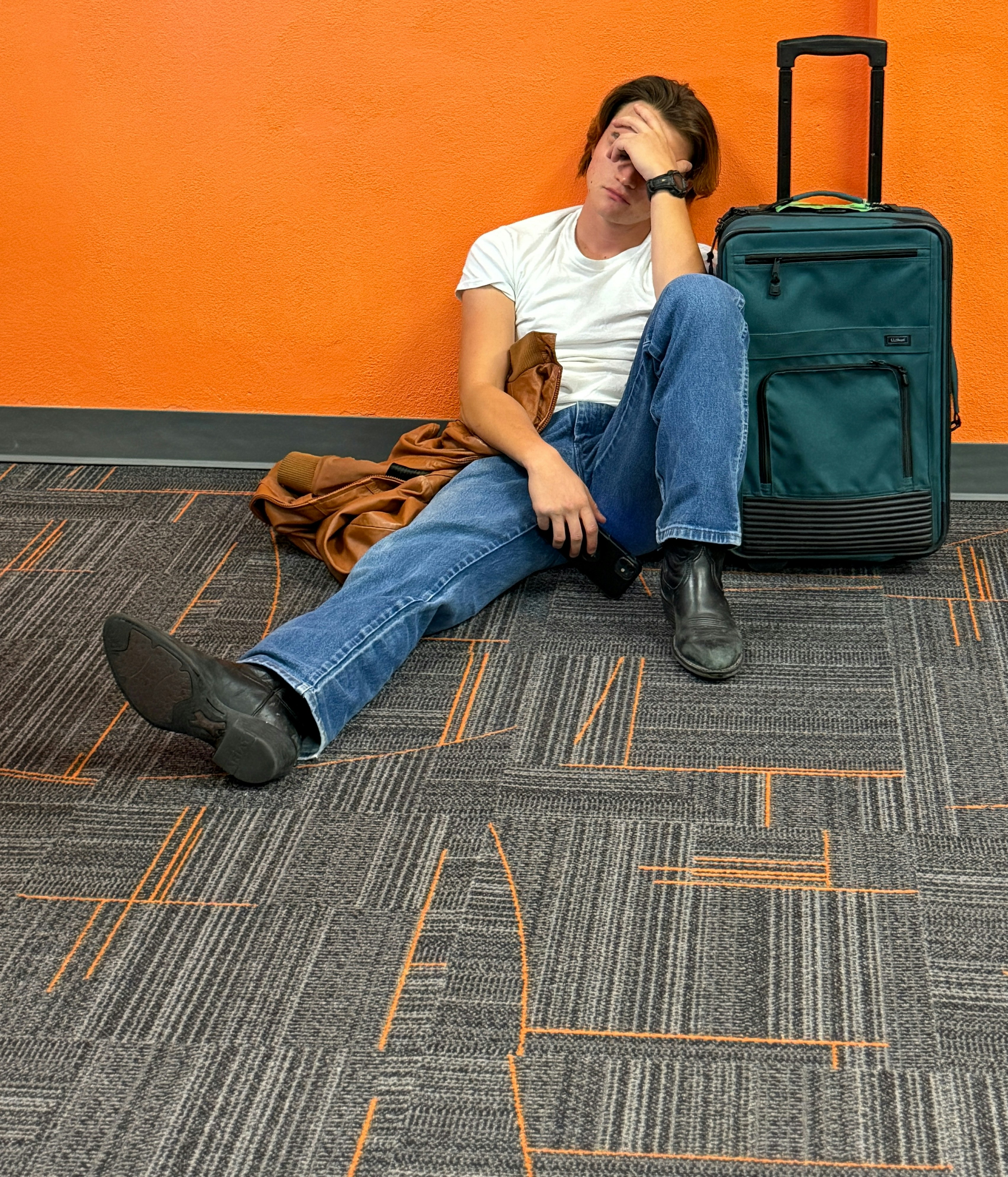 Man sitting on floor with luggage, looking tired.