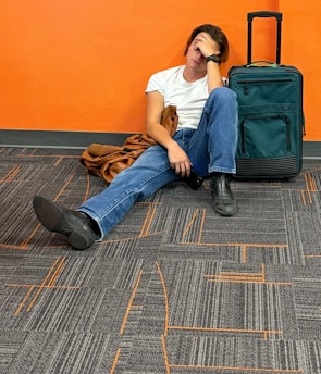 Man sitting on floor with luggage, looking tired.