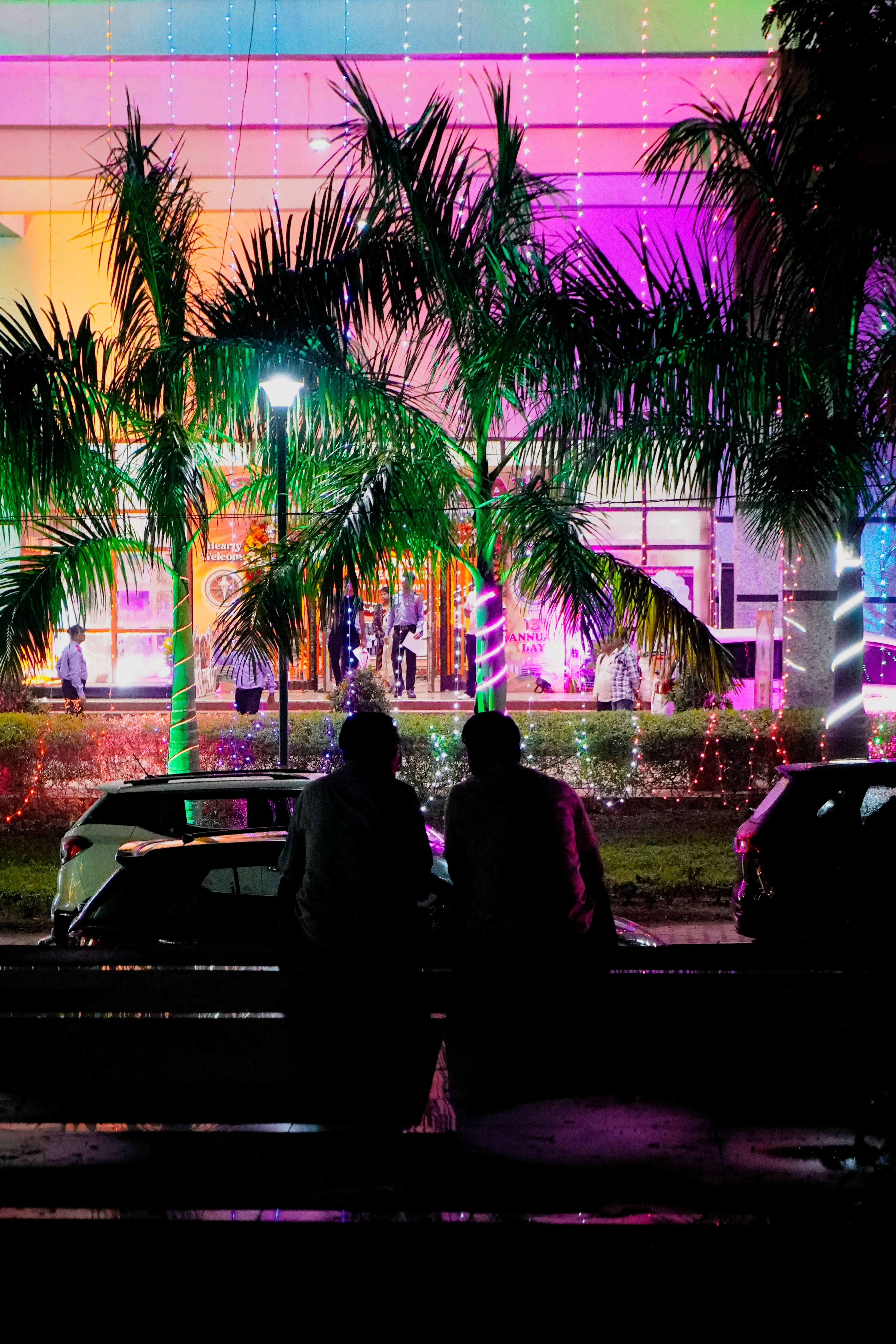 Two people silhouetted against a brightly lit building at night.