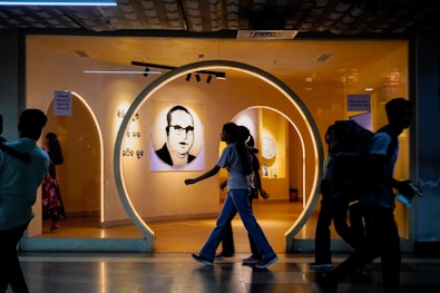 People walk past an illuminated exhibit entrance with a portrait.